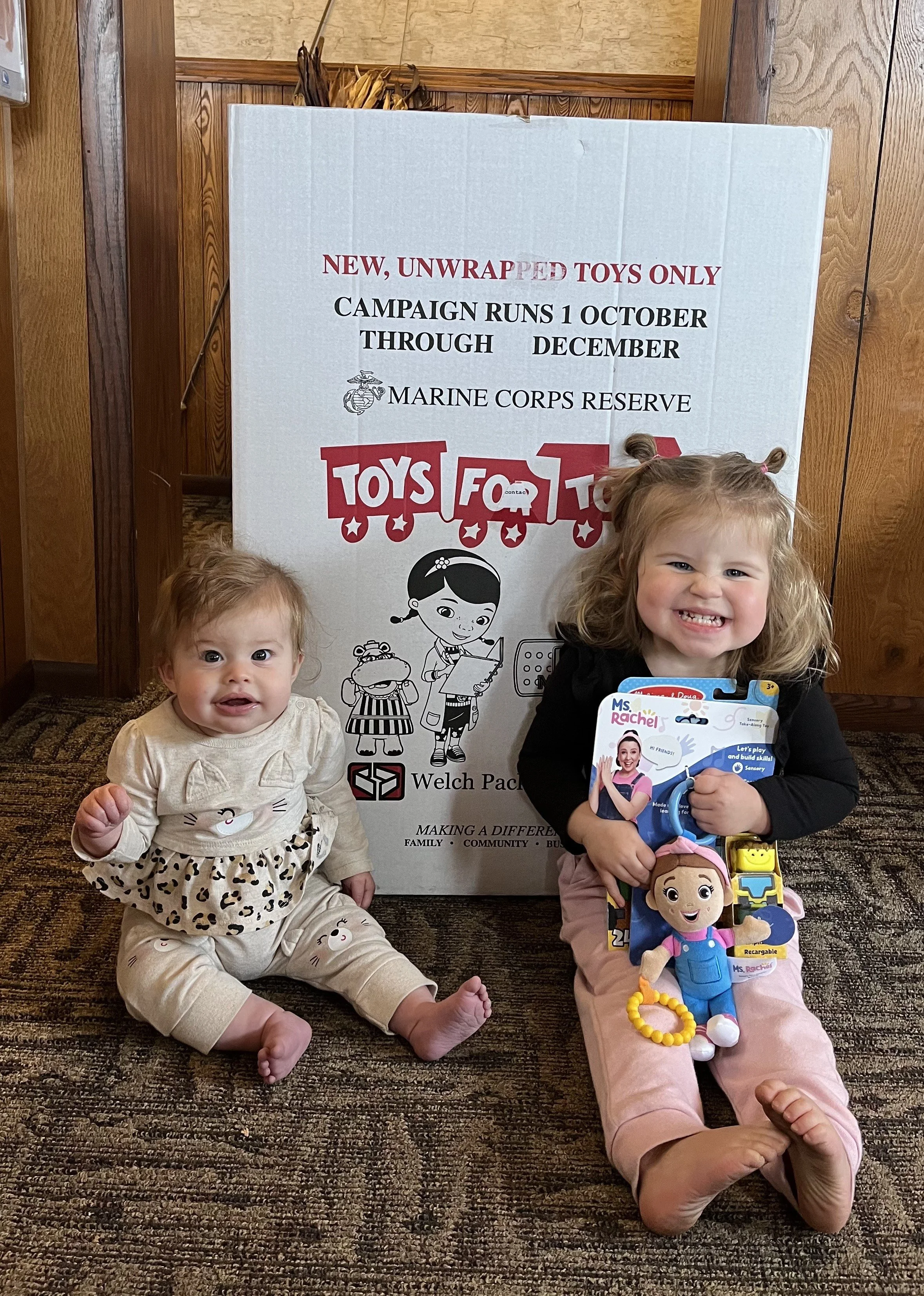 The daughters of Dr. Isaiah posing with the Shawano County Toys for Tots box in our office