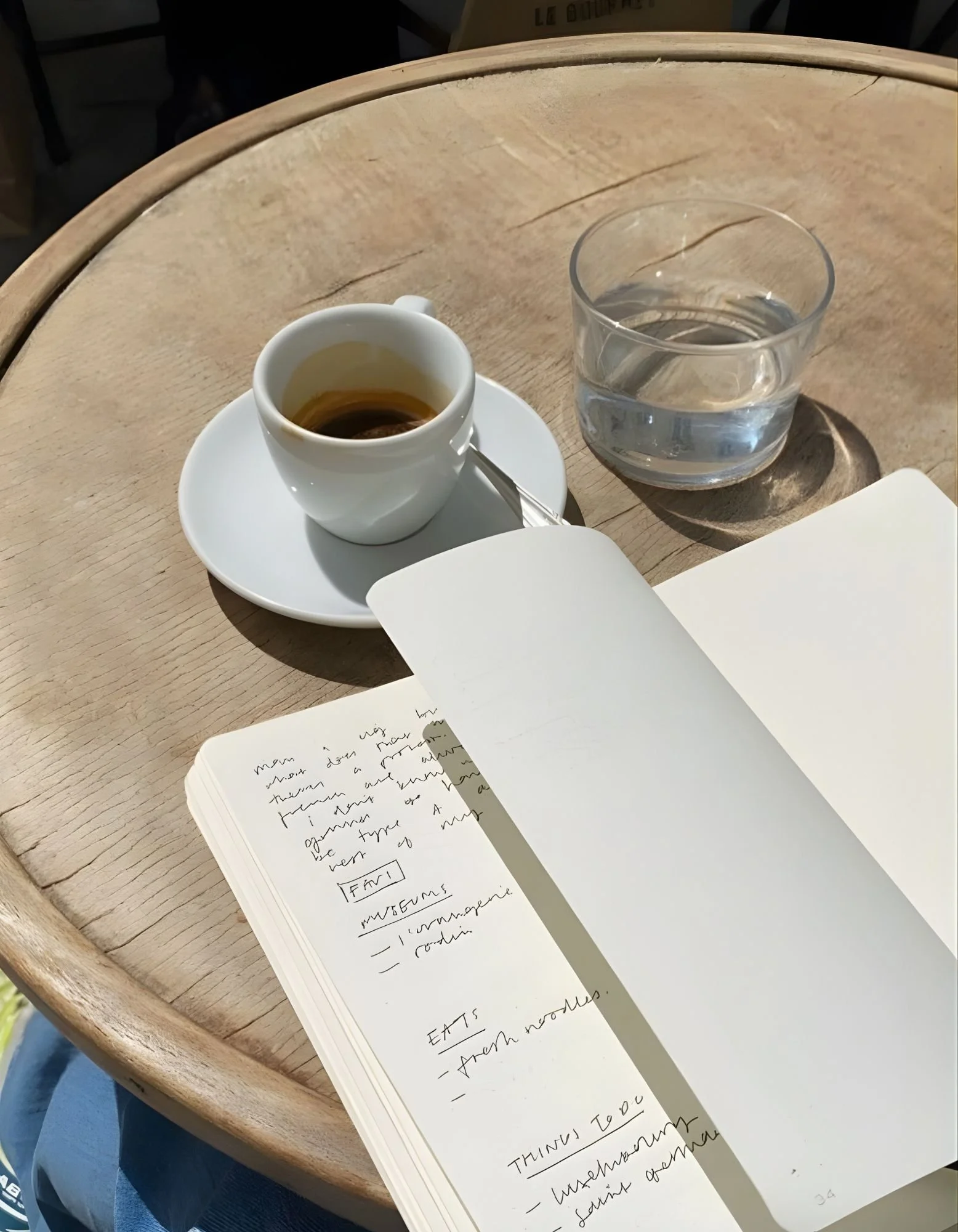 A cup of espresso, a glass of water, and an open journal on a wooden table representing thoughtful journaling and intentional living