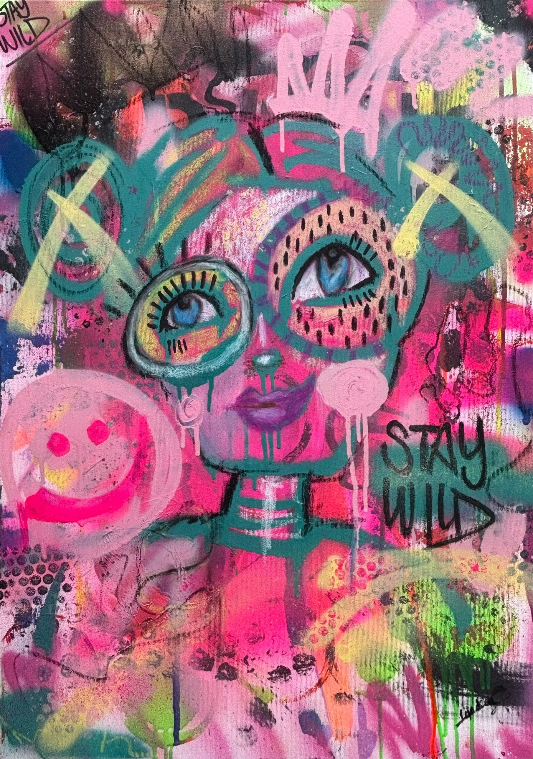 A vibrant graffiti-style painting featuring a cartoonish female face with large eyes and purple lips. The artwork includes abstract shapes, bright colors such as pink, green, blue, and yellow, and text that reads "STAY WILD." There are various doodle