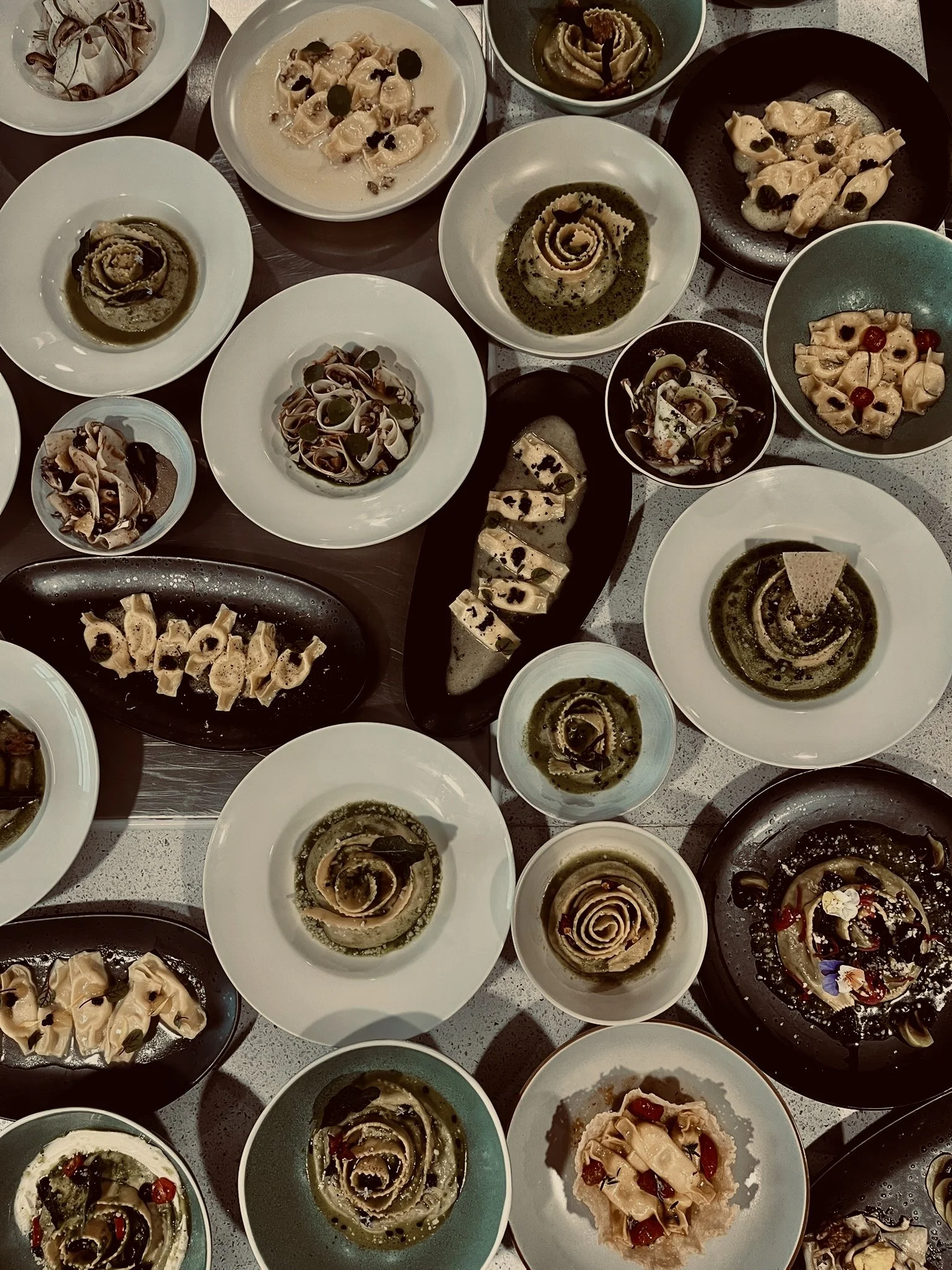 A variety of plates and bowls with different types of pasta, including ravioli, tortellini, and fettuccine, garnished with herbs, sauce, and herbs.