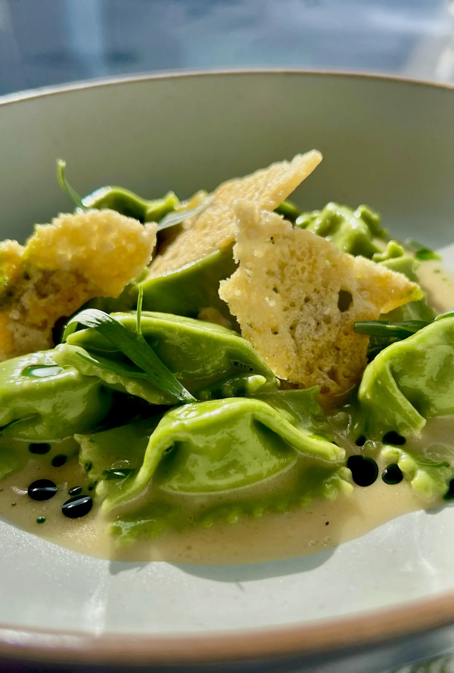 Close-up of a bowl of green soup with leafy greens, topped with crispy crackers and black sesame seeds.