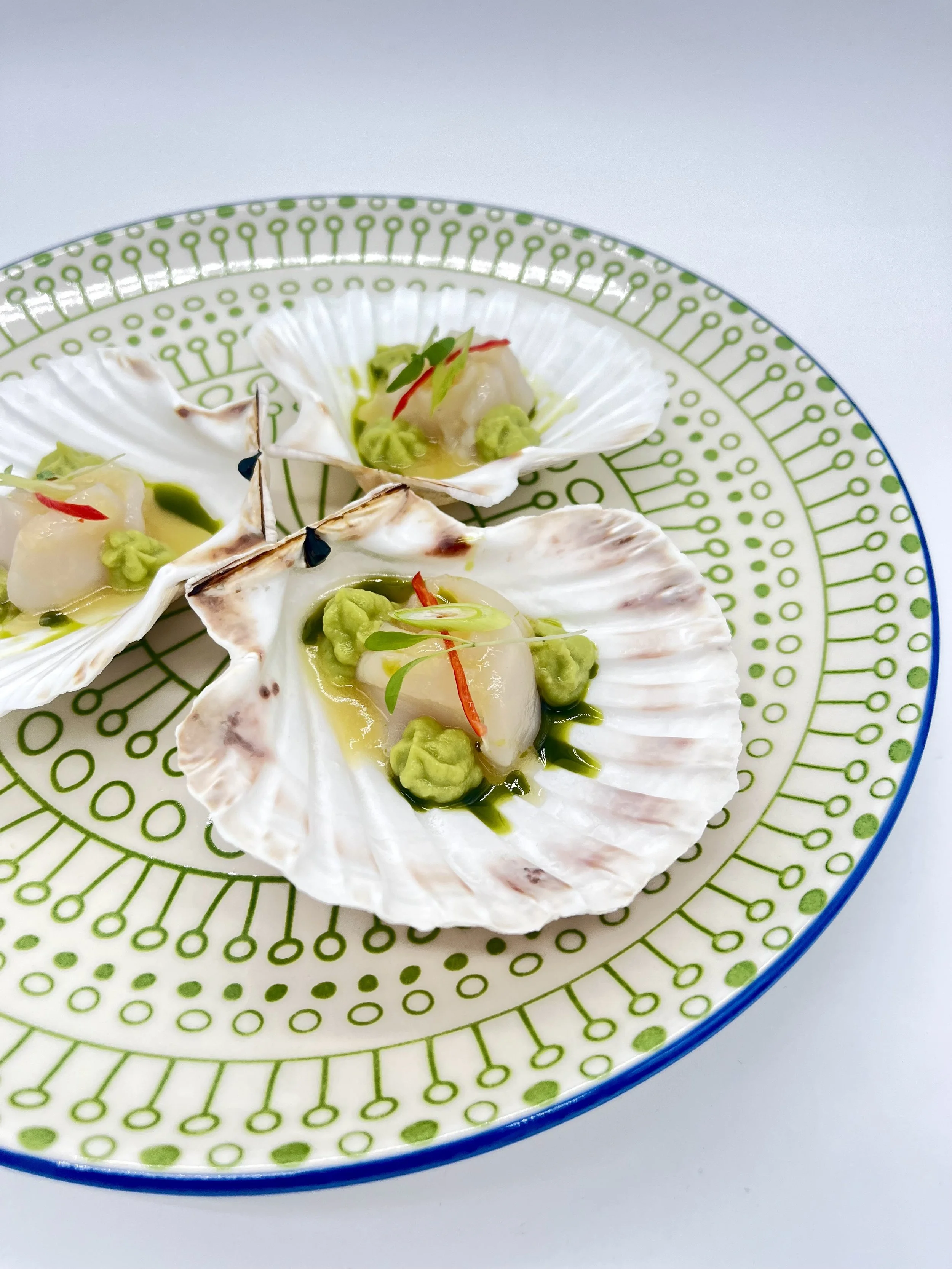 Seafood dish featuring shellfish served on a decorative green and white plate with garnishes.