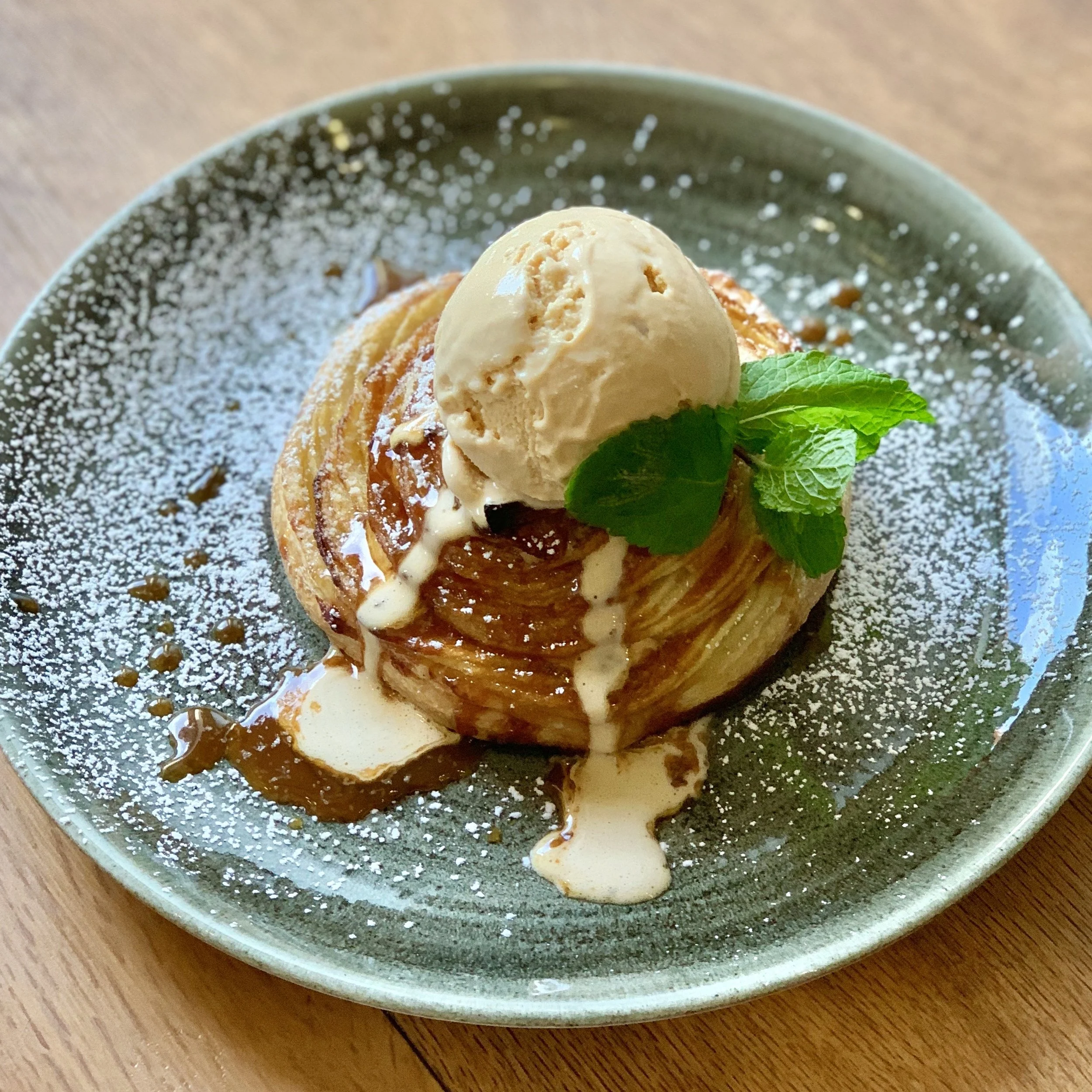 Dessert with a pastry topped with vanilla ice cream, caramel sauce, whipped cream, and mint leaves, dusted with powdered sugar