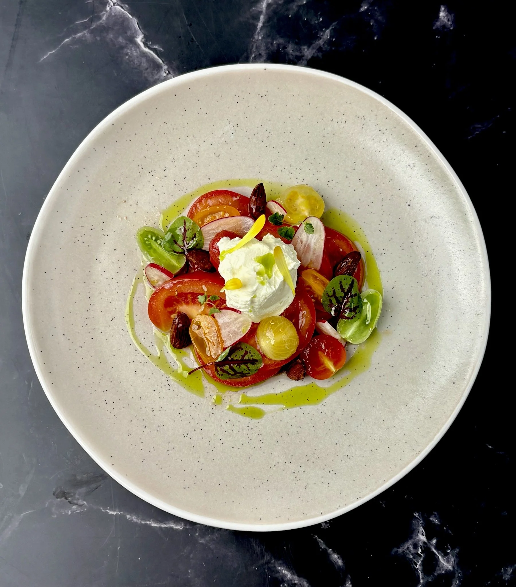 Salad with cherry tomatoes, microgreens, dollop of goat cheese, and a drizzle of green vinaigrette on a white plate.