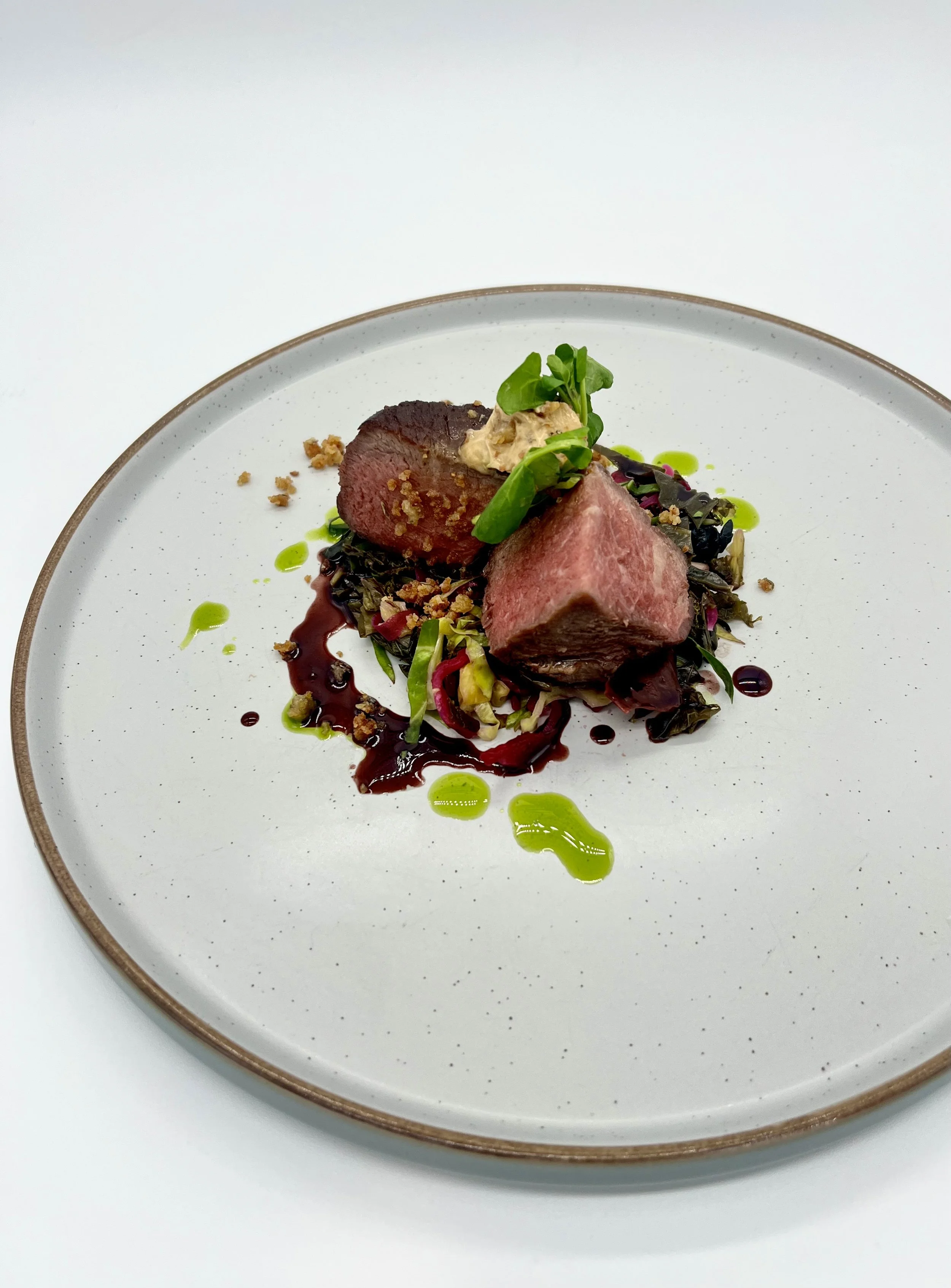 Premium plated beef dish with sauce and greens on a white speckled plate