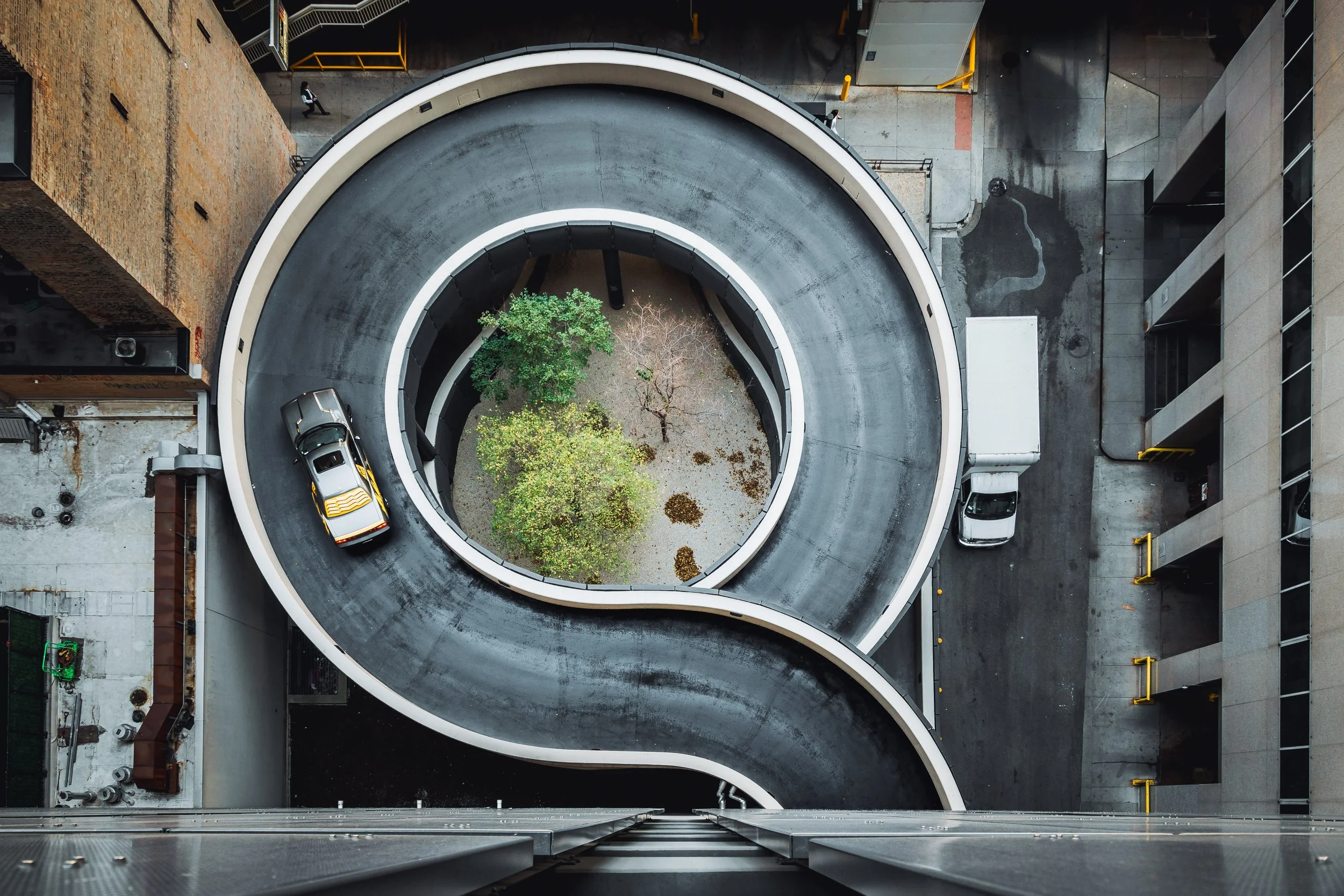 Bird's-eye view of a spiral parking garage with a car driving on the ramp.