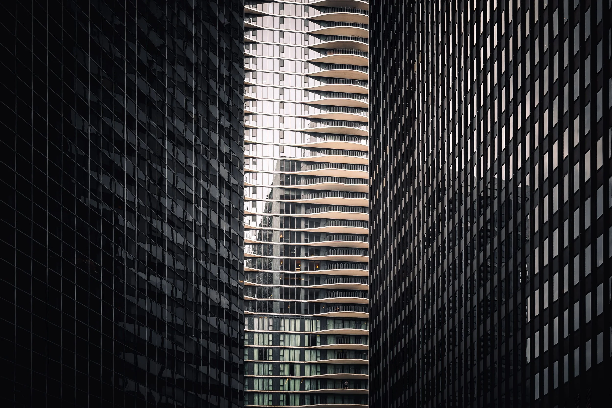 View of tall modern city buildings with glass facades, including a cylindrical building with curved balconies in the background.