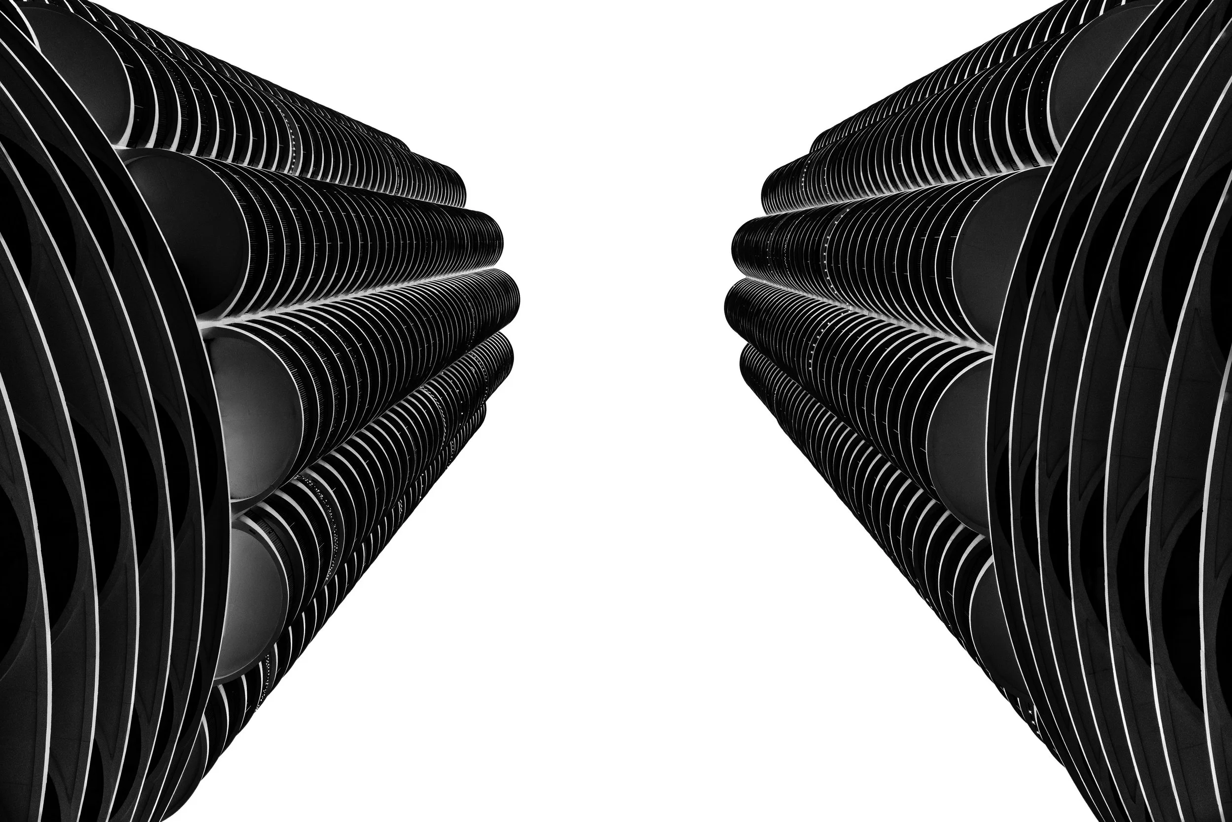 Black and white upward view of two modern skyscrapers with curved, layered facades against a white sky.