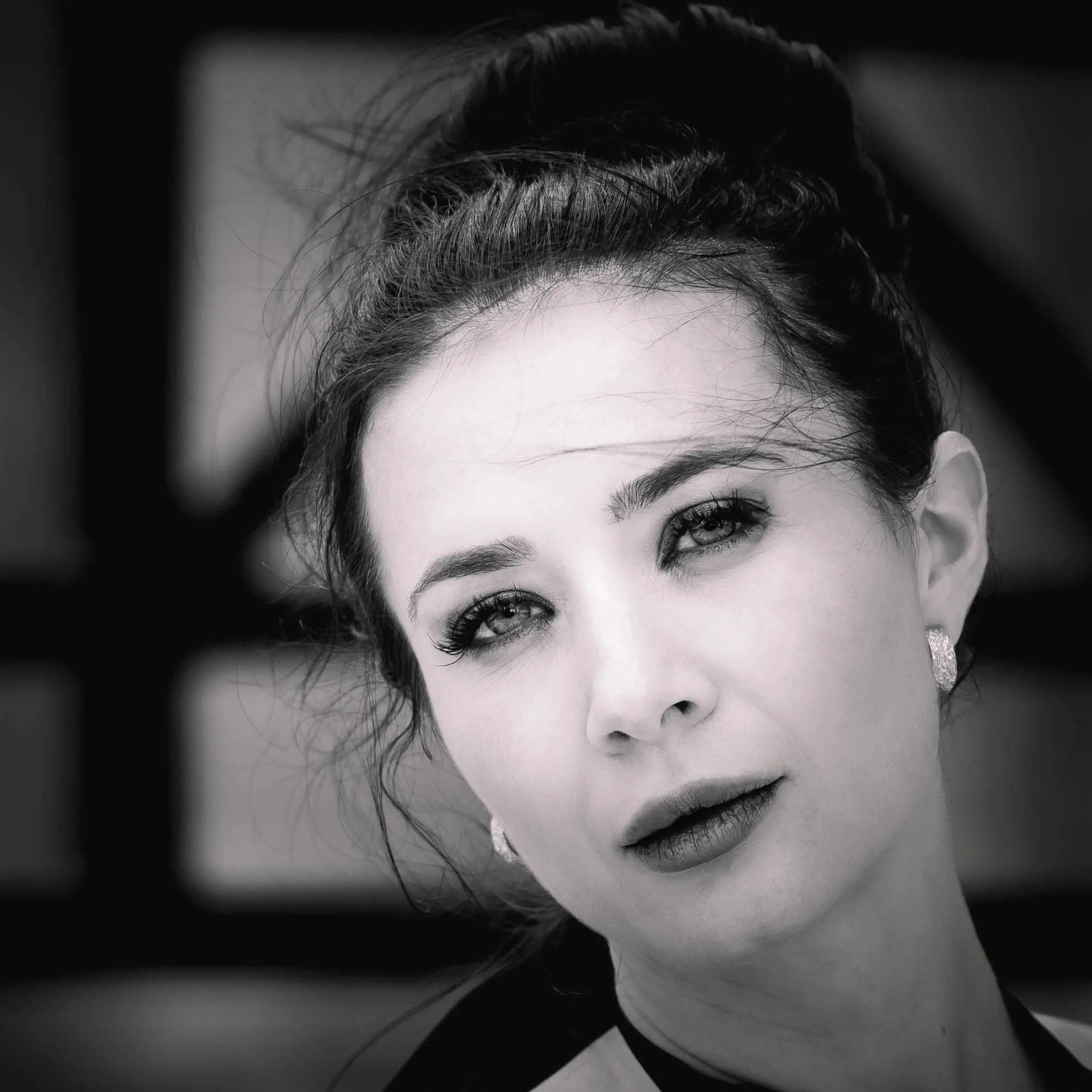 Close-up black and white portrait of a woman with styled hair and jewelry, looking into the camera.