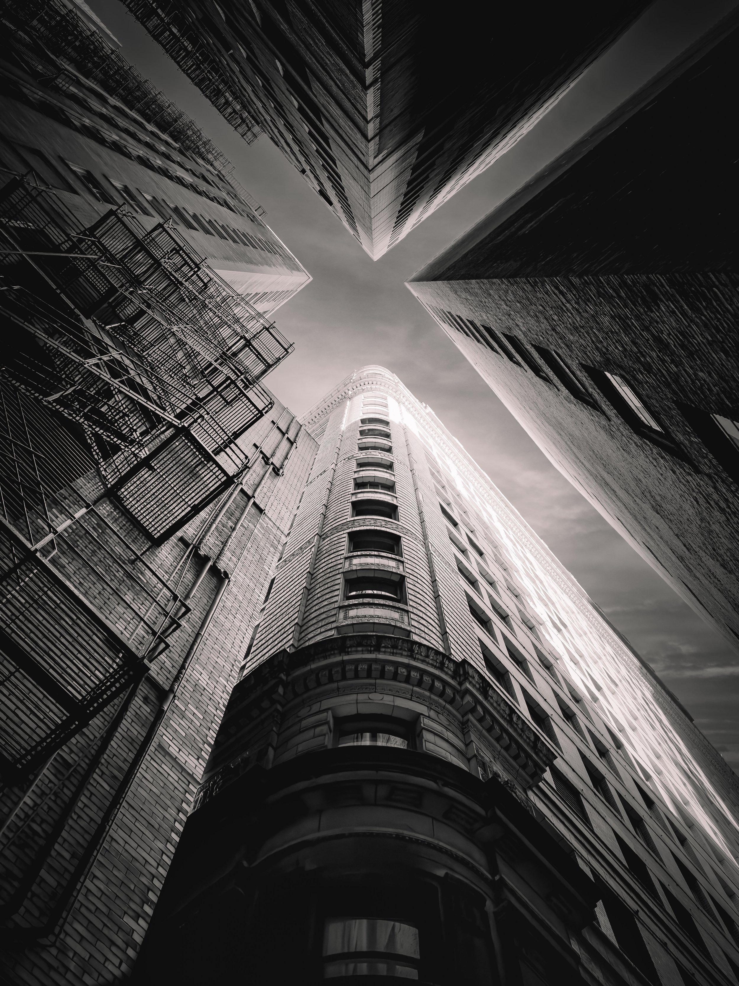 Low-angle black-and-white photo of tall skyscrapers seen from street level, converging towards the sky.