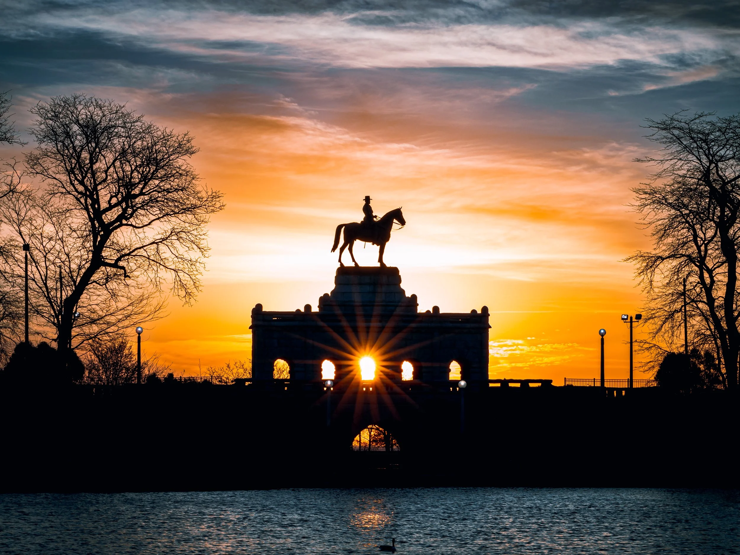 Silhouette of the Ulysses S Grant statue at sunrise with a body of water in the foreground.
