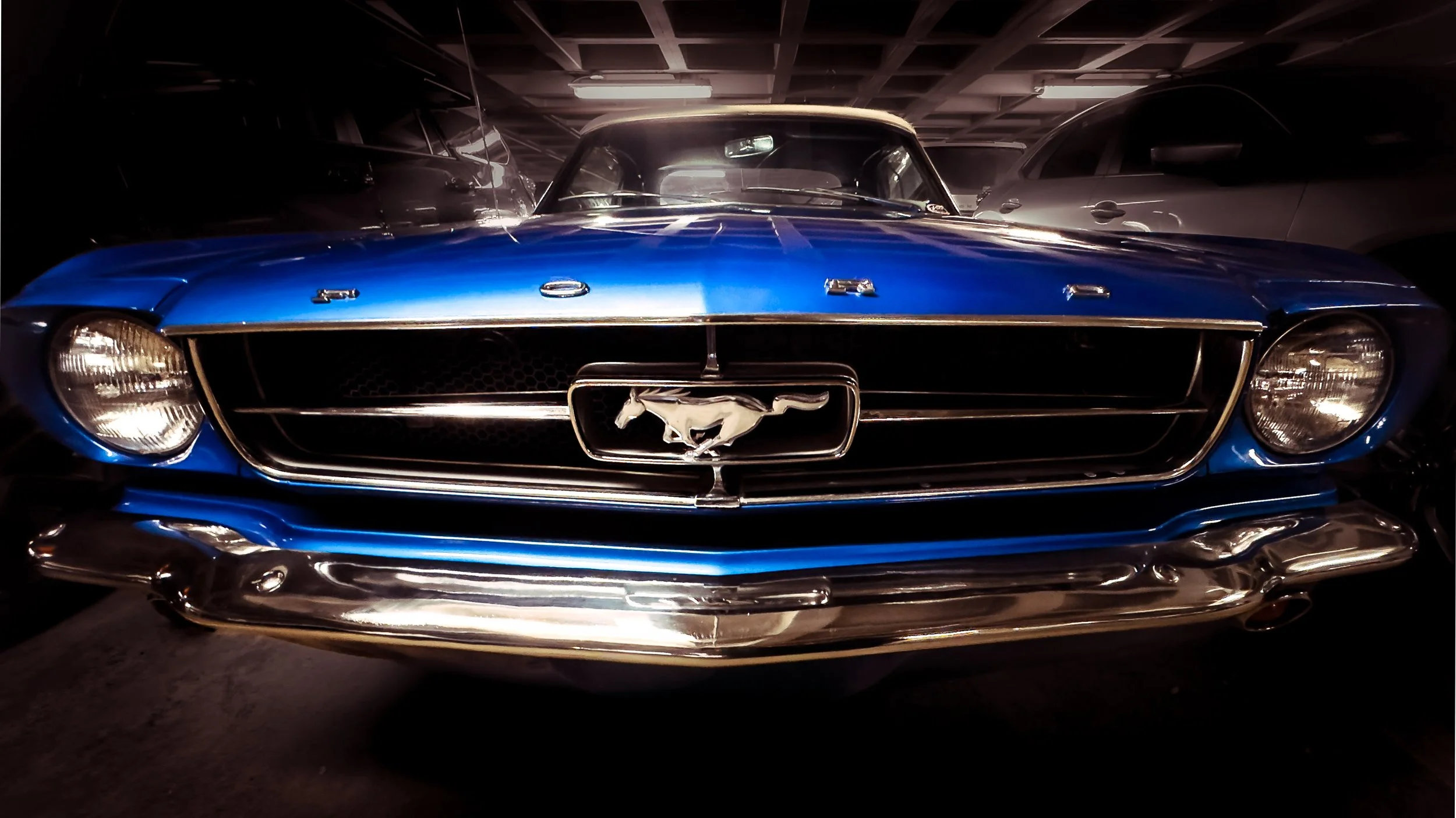 Front view of a vintage blue Ford Mustang car in a parking garage.
