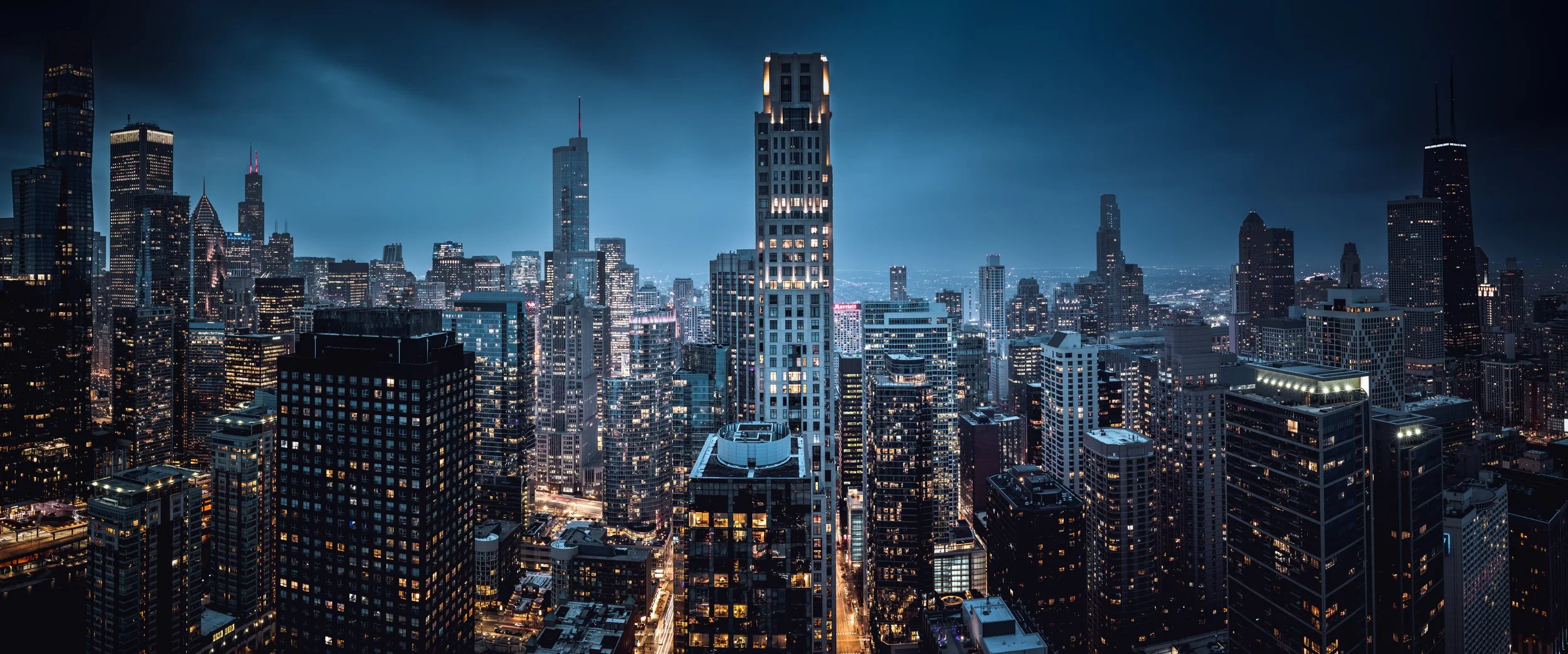 Nighttime aerial view of a city skyline with illuminated skyscrapers and dark skies.