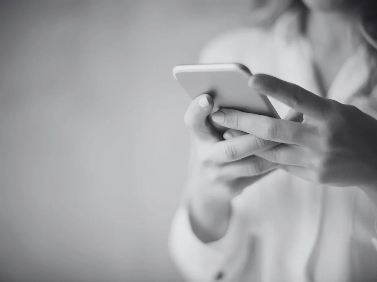 A person holding a smartphone with one hand, scrolling or tapping on the device, in black and white.