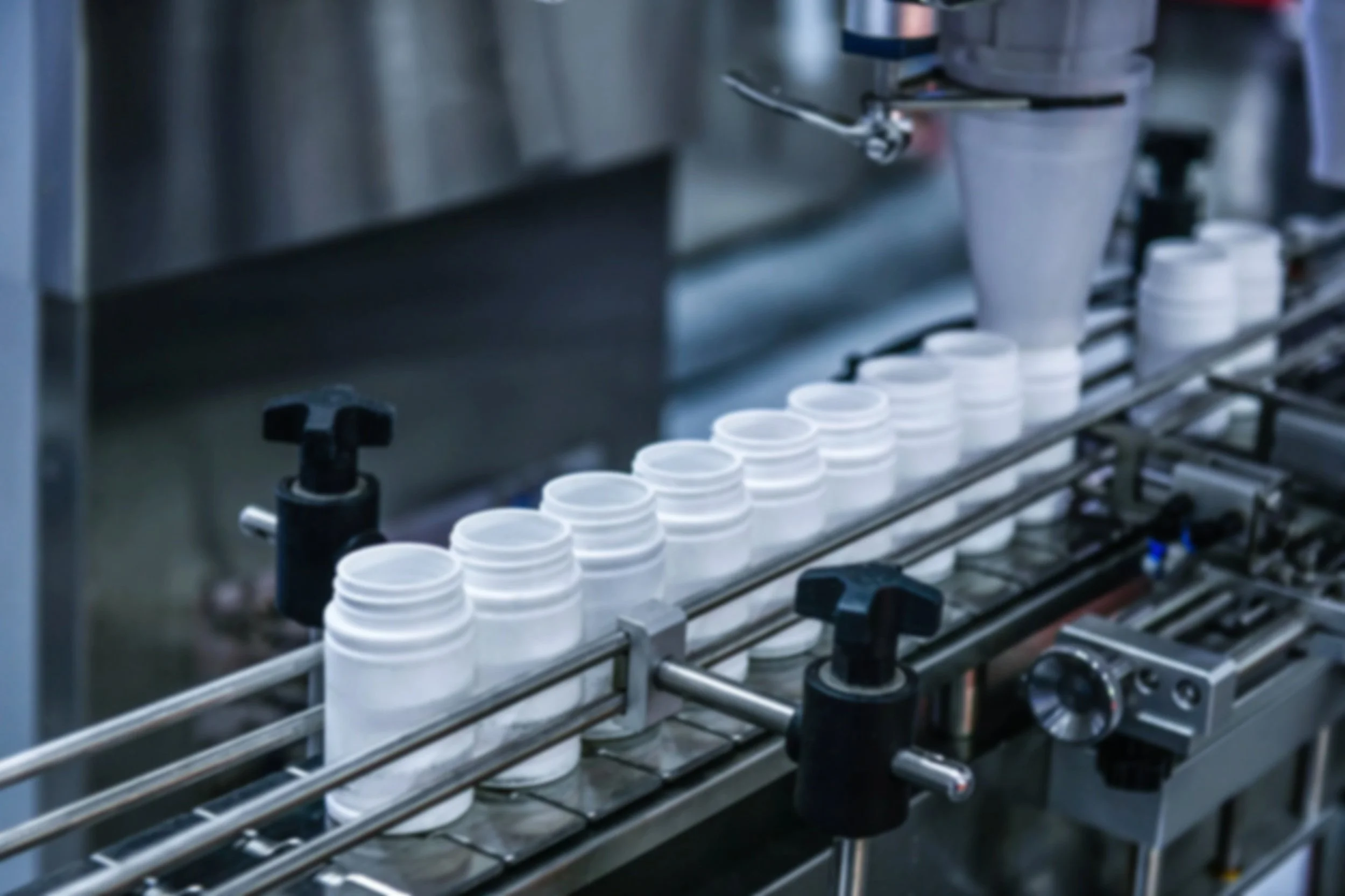 A conveyor belt in a manufacturing facility with empty white plastic containers moving along.