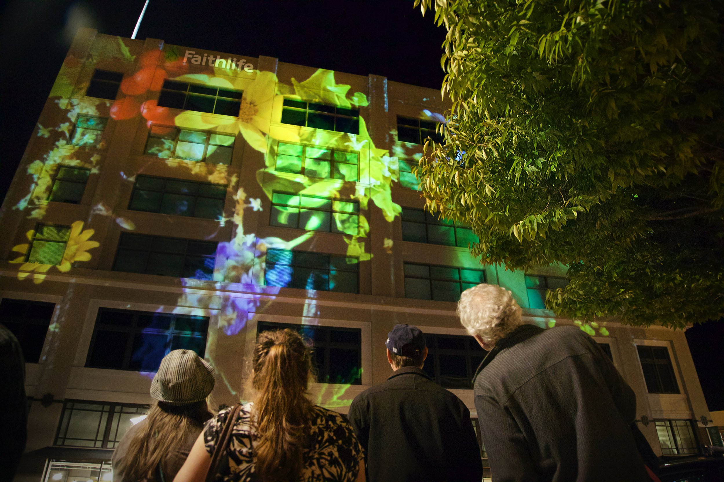Faithlife projection mapping in downtown Bellingham, crowd watching floral visuals light the facade from below.