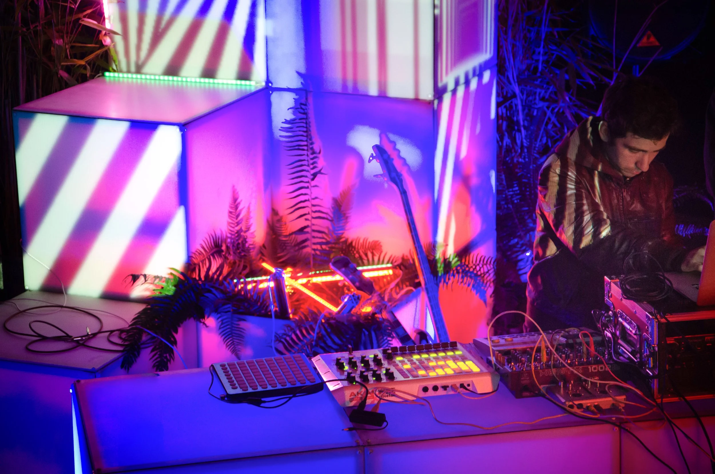 Lighting design event control booth, an illuminated cube backdrop and DJ over a lit console and mixers