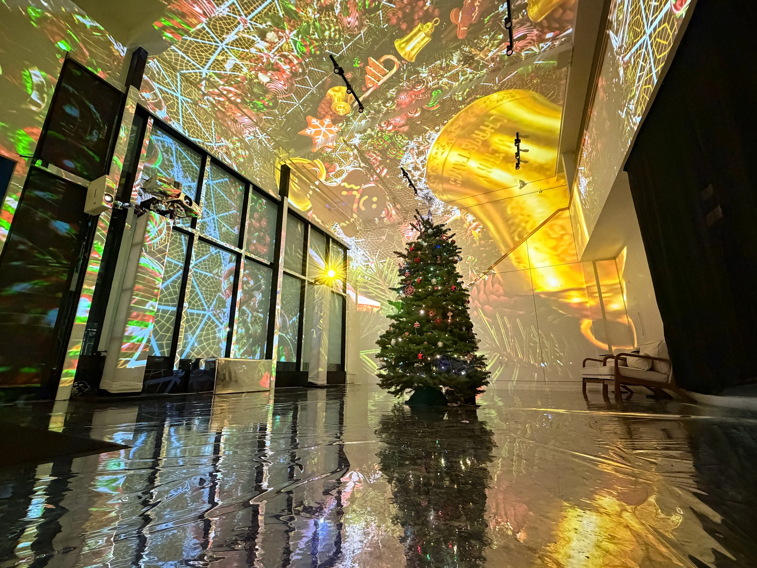 Holiday visuals by NOVA Light Labs, festive ornaments and gold bells mapped across a lobby around a lit tree.