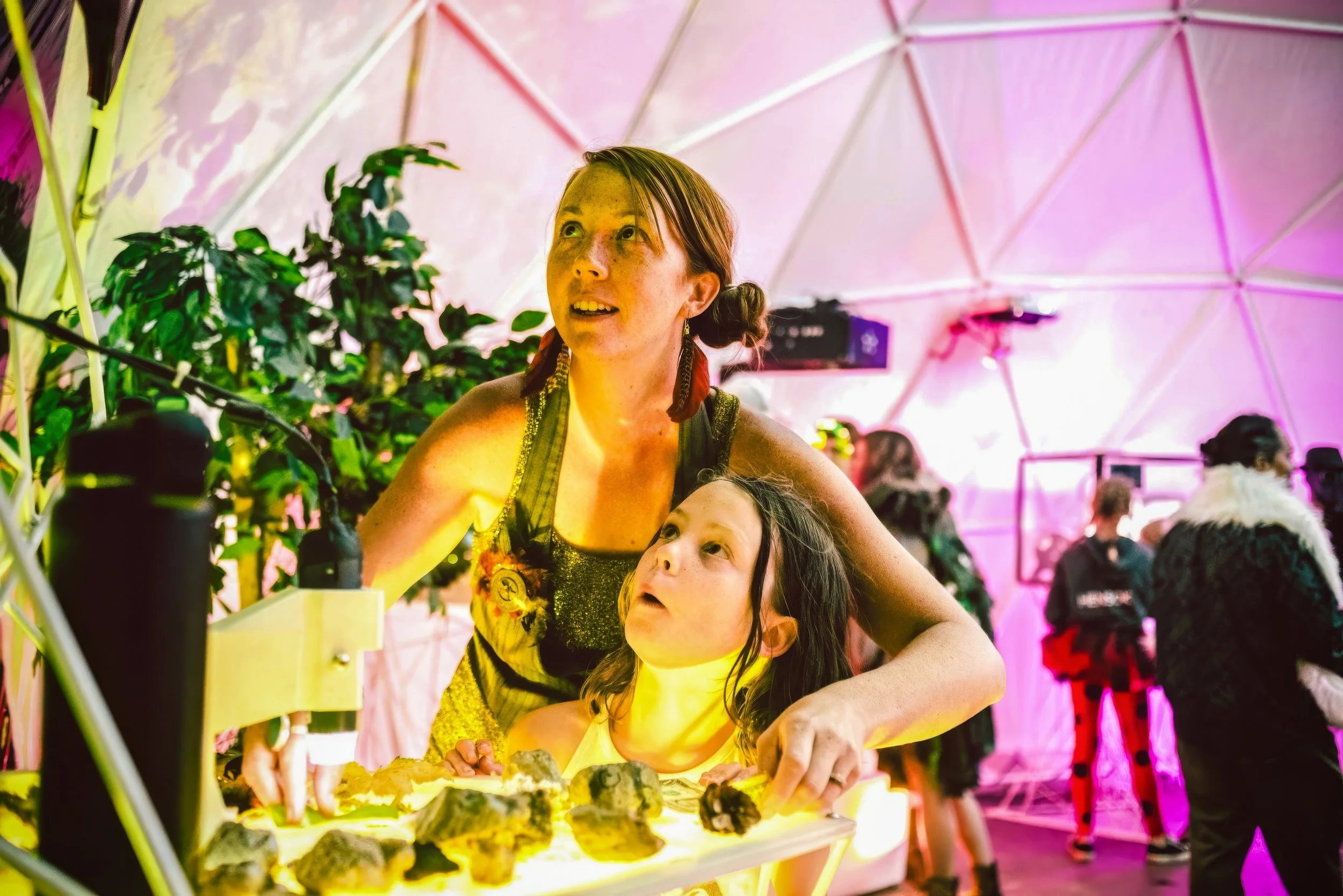 Sandbox of Life inside a geodesic dome, an adult and child looking up together from the lit sand table