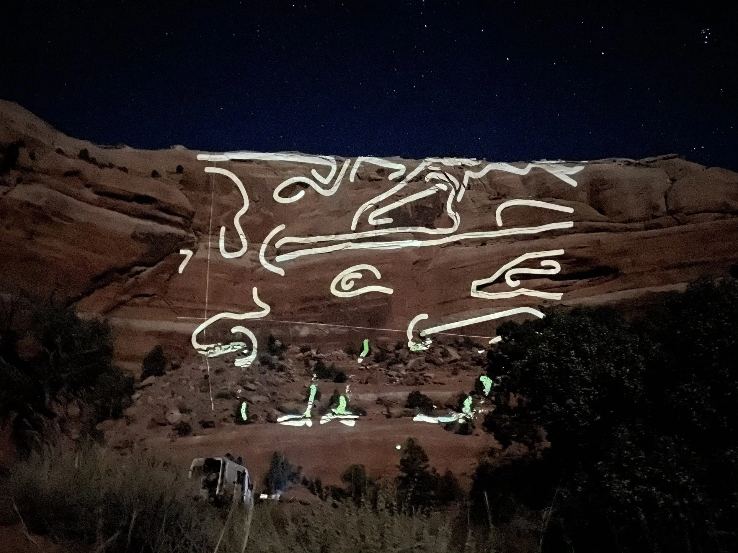 White line art projected on a red sandstone cliff outside Moab, Utah, under a starry sky.