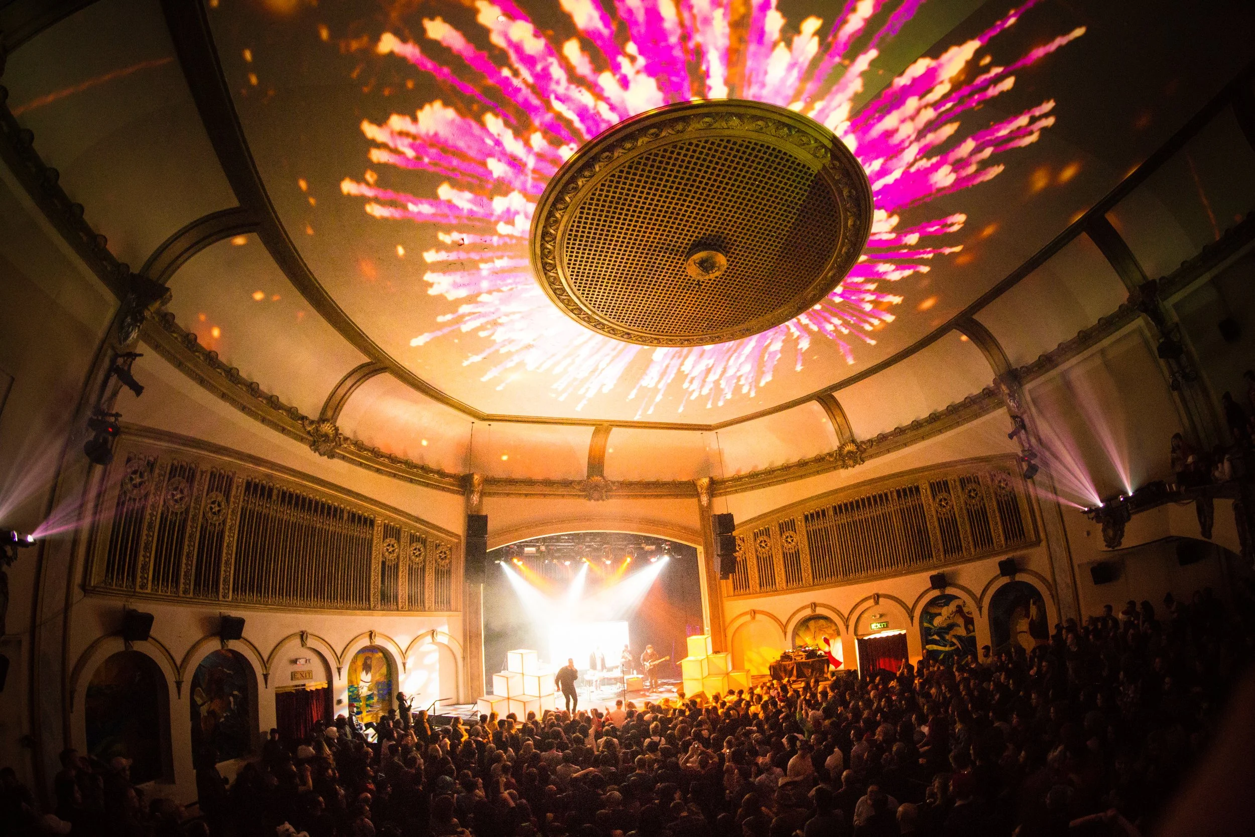 Projection mapping across a domed theater ceiling above a live band, pink burst radiating from the center vent