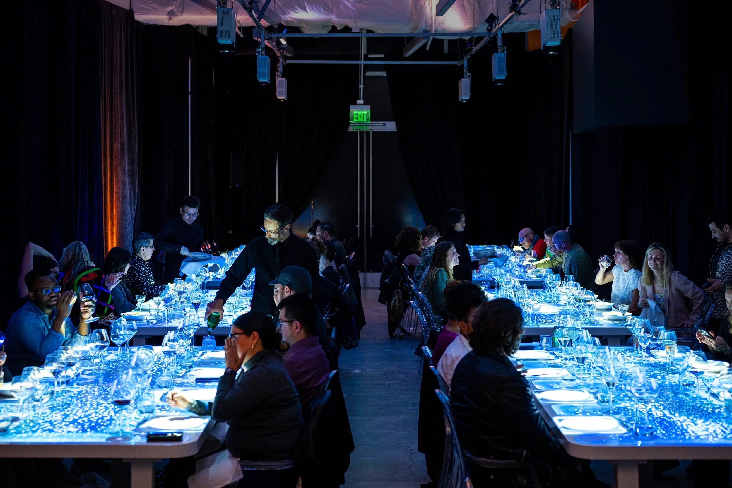 The Radiant Table projection mapping system, long blue mapped tables fill the darkened venue with guests