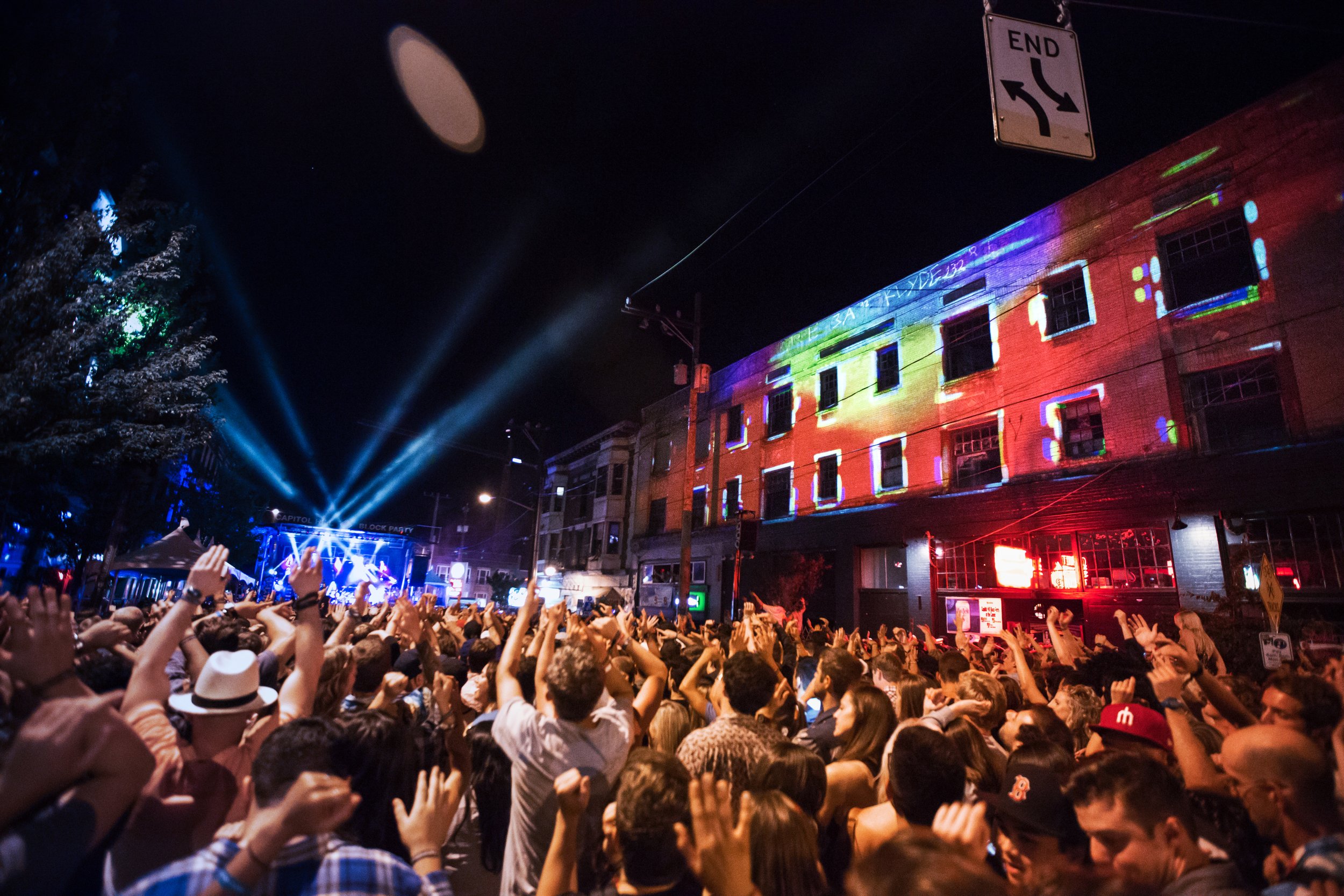 Projection mapping on a brick building facade at an outdoor street concert, crowd with hands raised