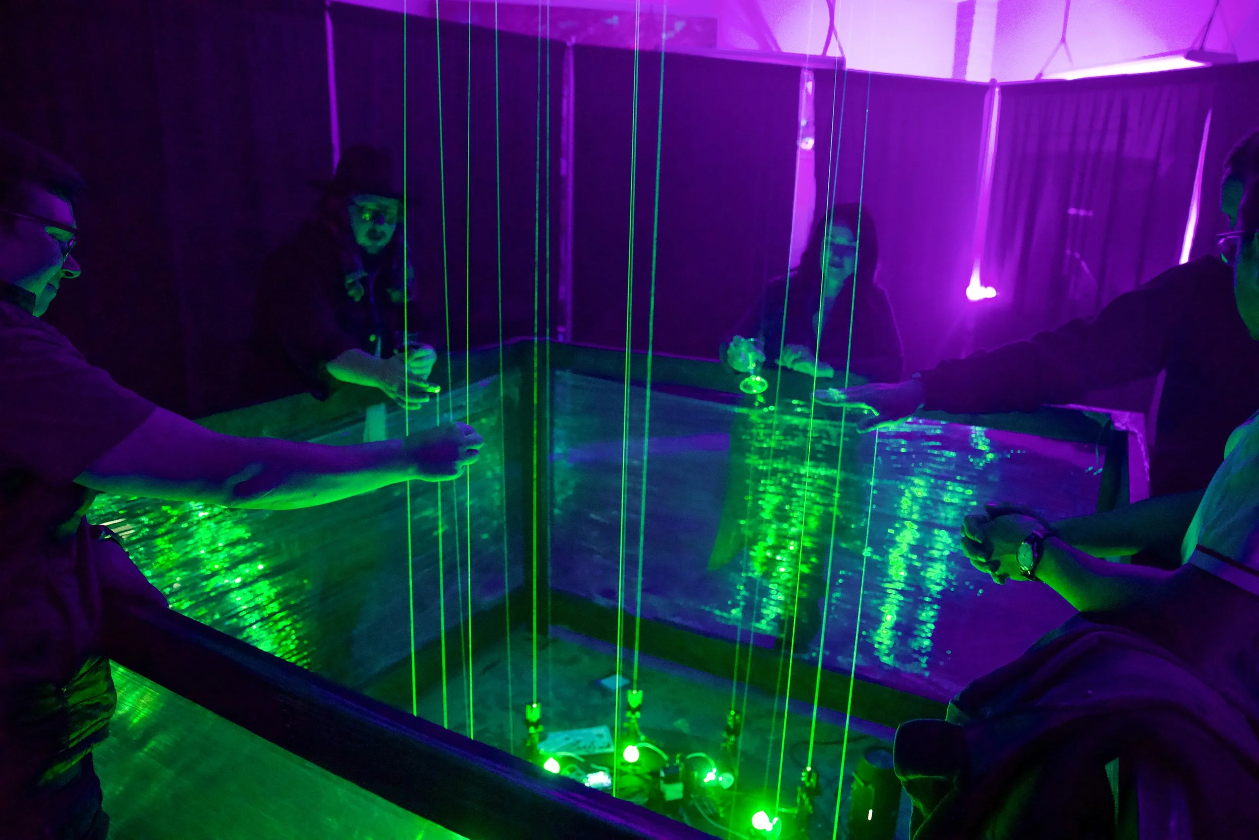 Guests playing the laser harp at ILLUMIBRATE 2025 in Boise, Idaho, green beams falling in a ring under purple light.