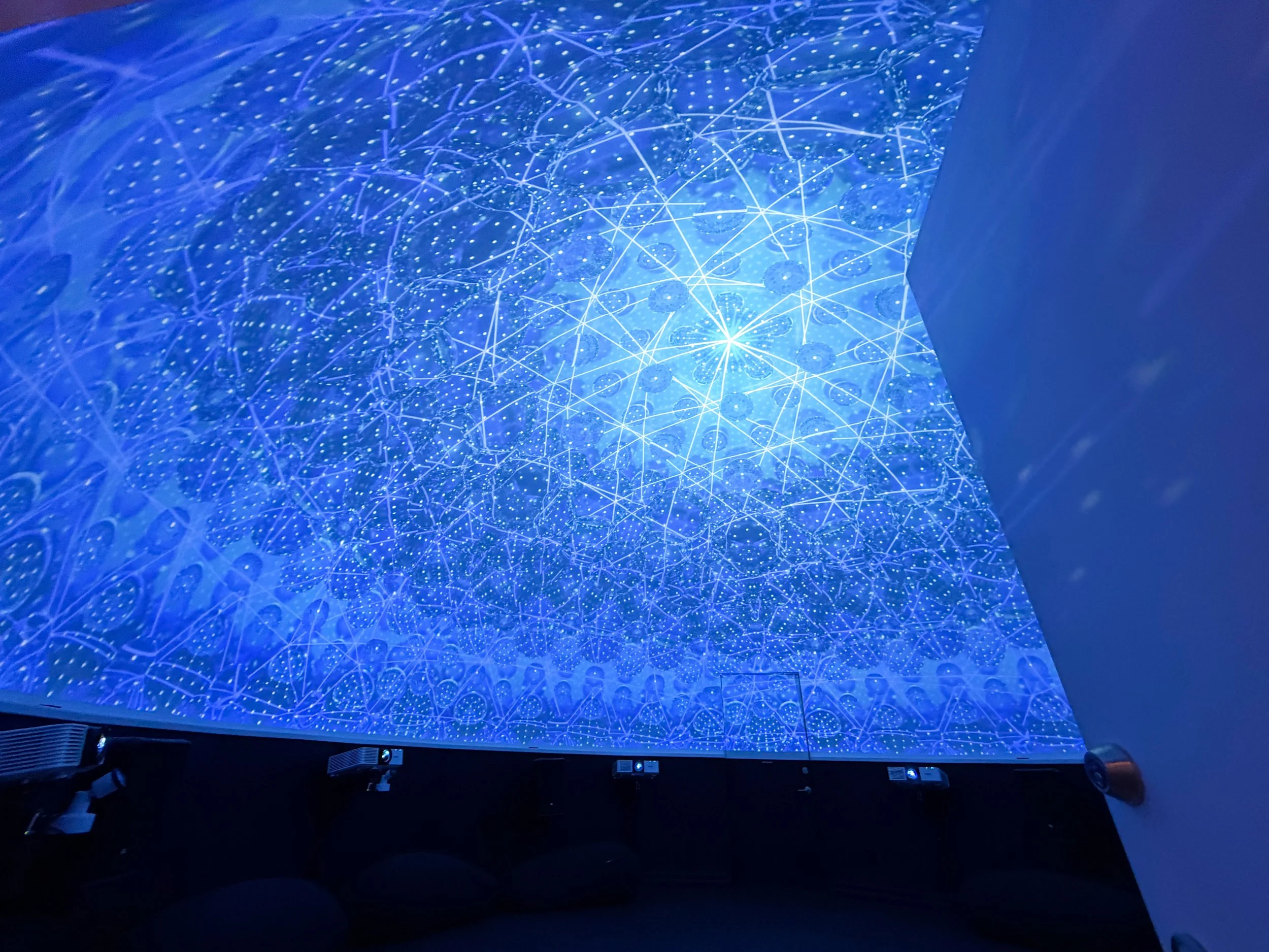 Immersive projection mapping dome glowing blue with a radiant web of stars and lace, projectors lined along the base