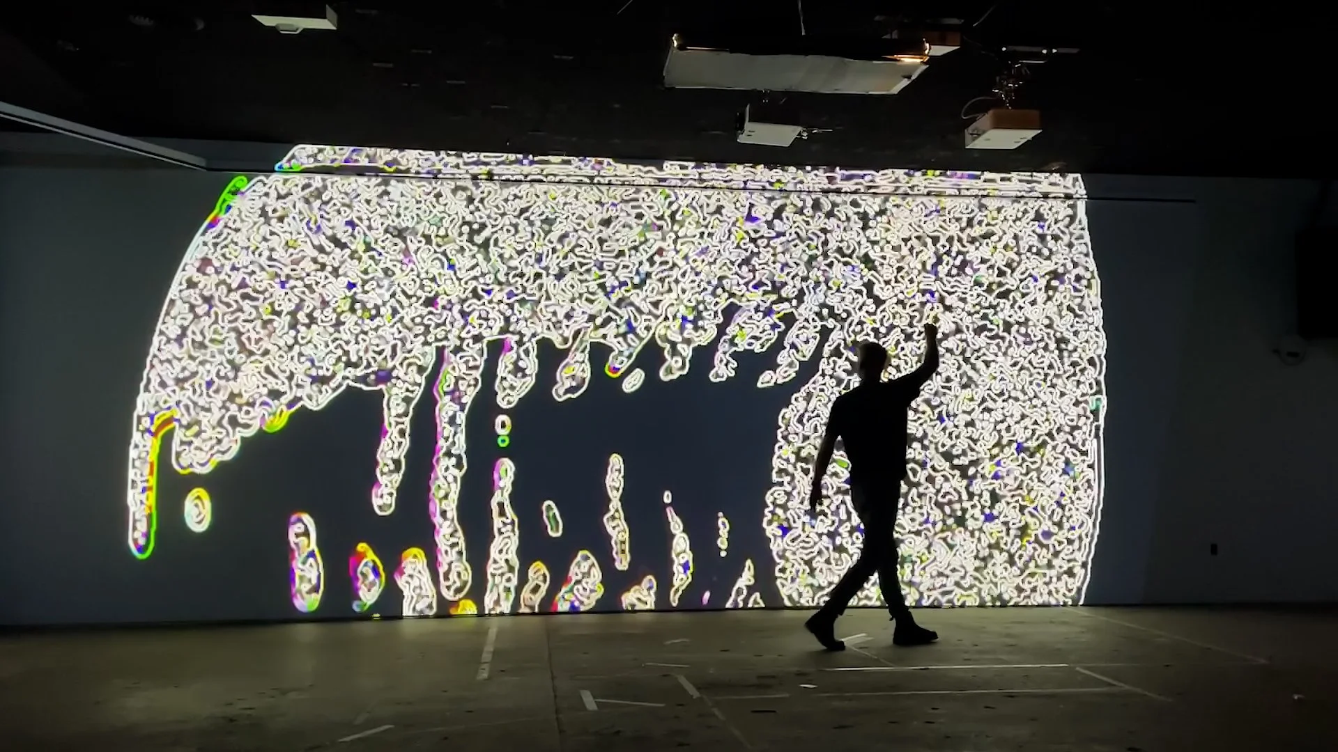 Silhouetted guest raises a laser at glowing white video feedback texture dripping down the projection wall