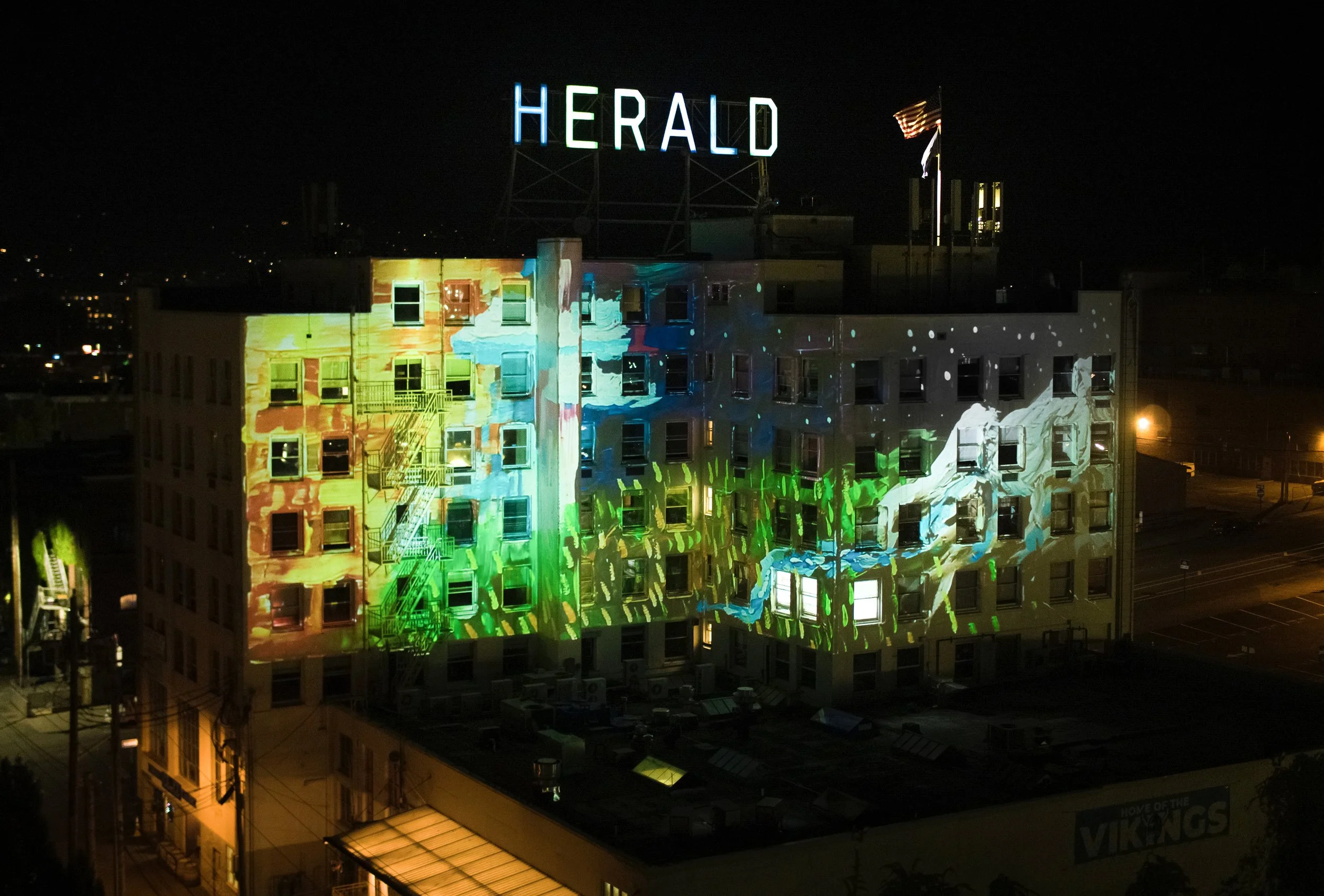 The Herald projection mapping in Bellingham, facade washed in amber, green, and blue across 5 stories at night.