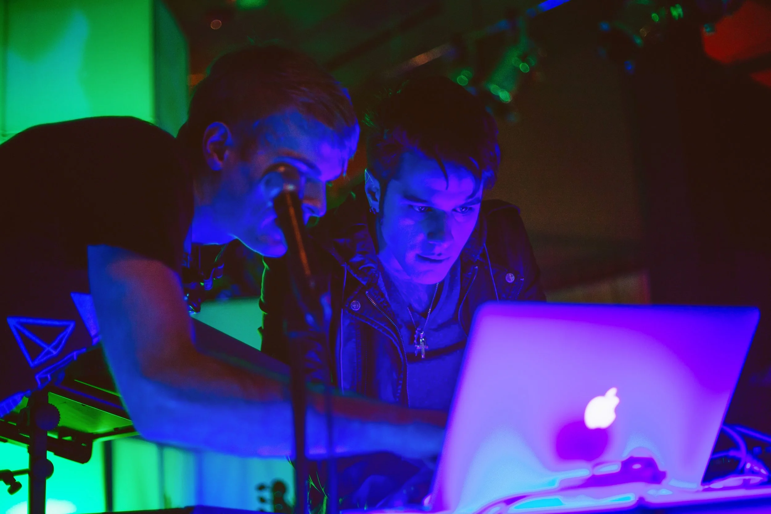 Two guests at a laser interaction station lit in blue and green, one sighting down the beam at a laptop