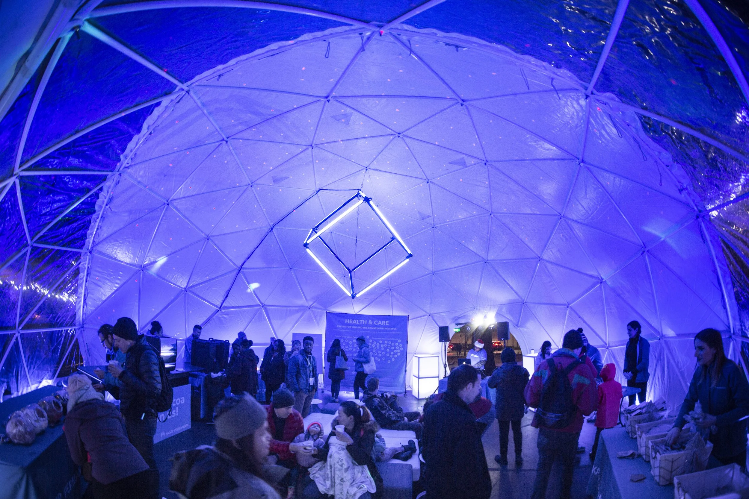 Interior of geodesic event dome in Seattle with guests under blue light and a cube chandelier of LED bars hung at center