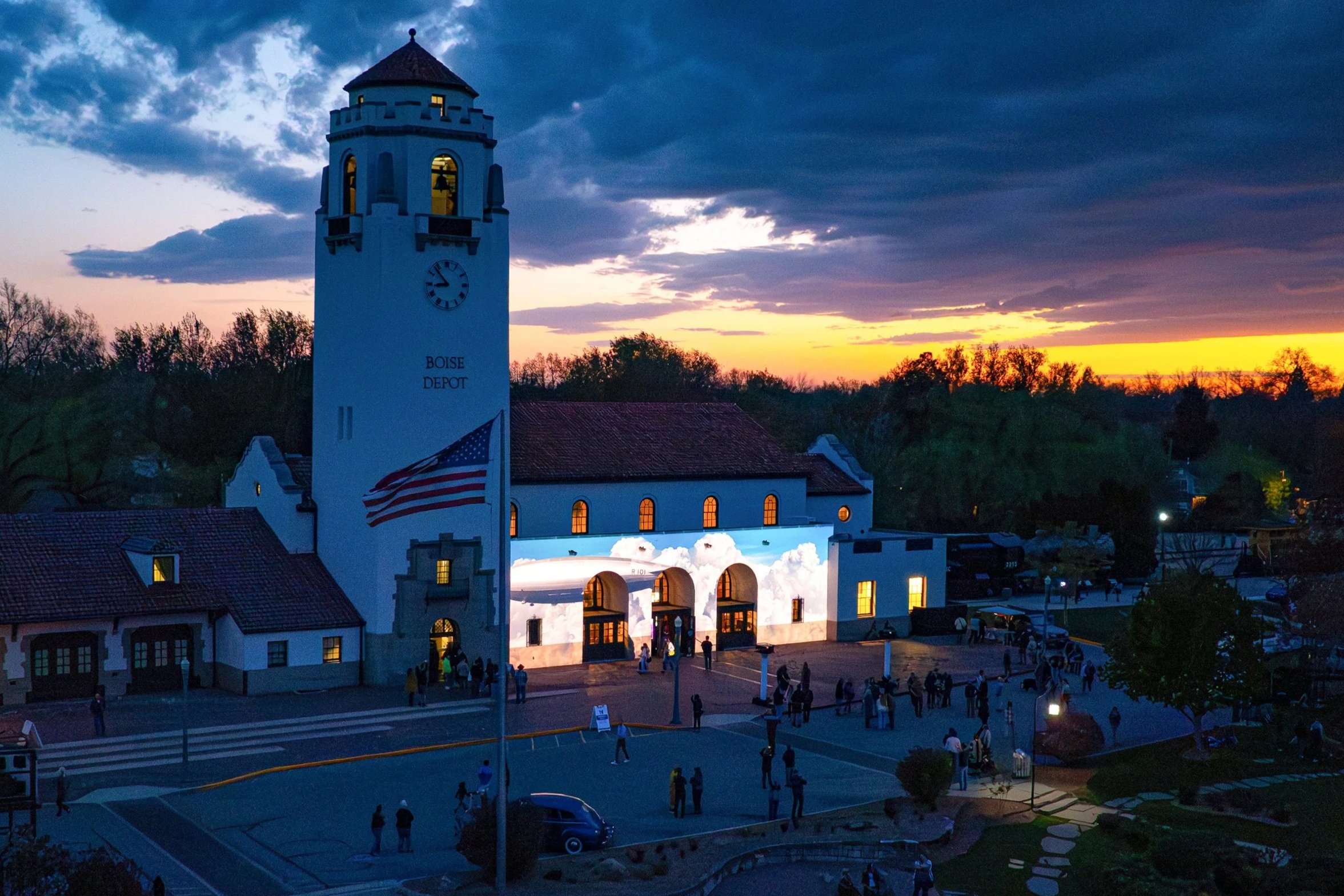 Architectural projection mapping on the Boise Depot at dusk, clouds washed across the arcade below the lit clock tower.