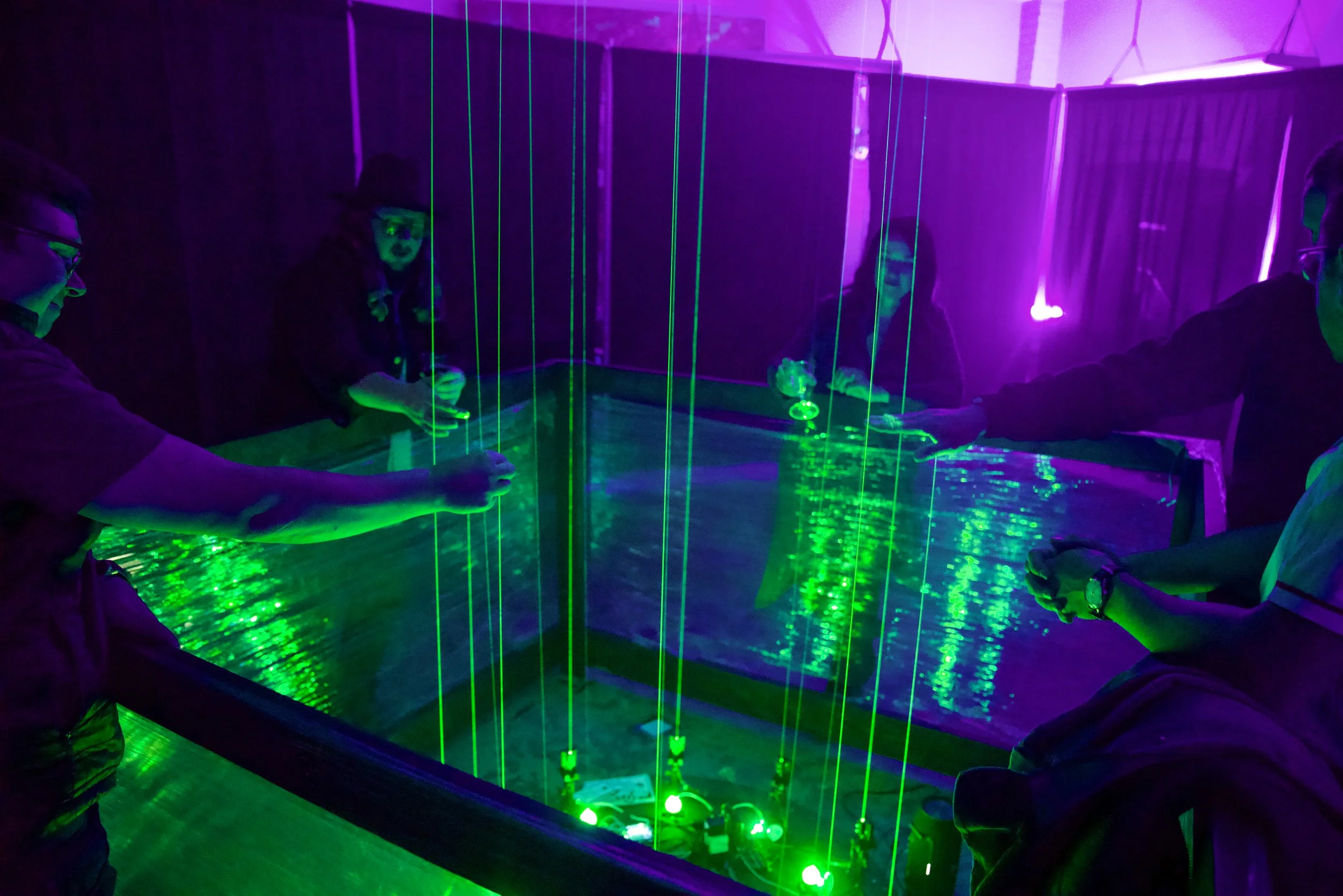 Guests reach through green laser harp beams inside a barrier at NOVA Light Labs installation, one holding a cocktail