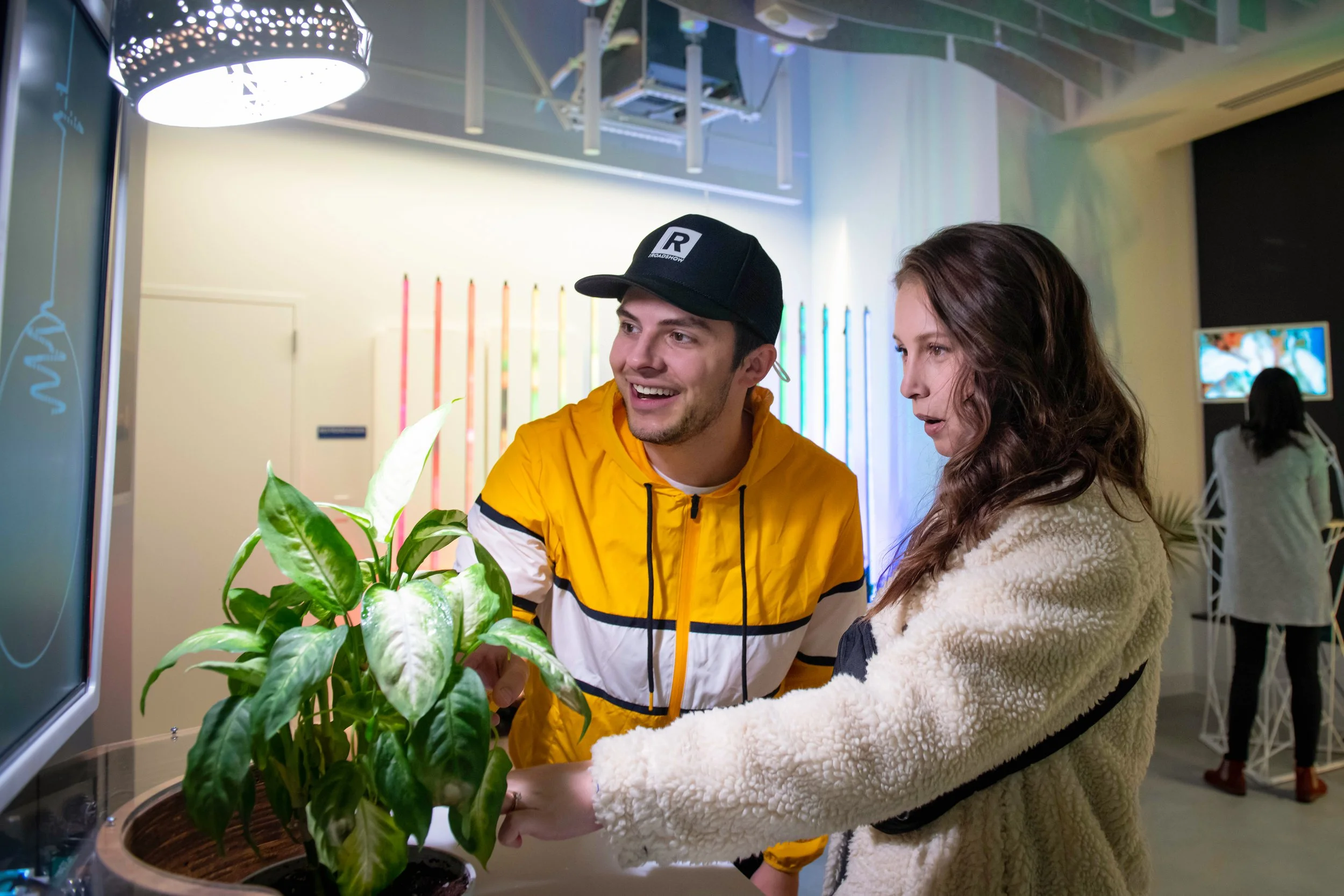 2 guests touching the Floragraph plant at Periodic Pop-Up in Seattle, a waveform drawing on the screen beside it.