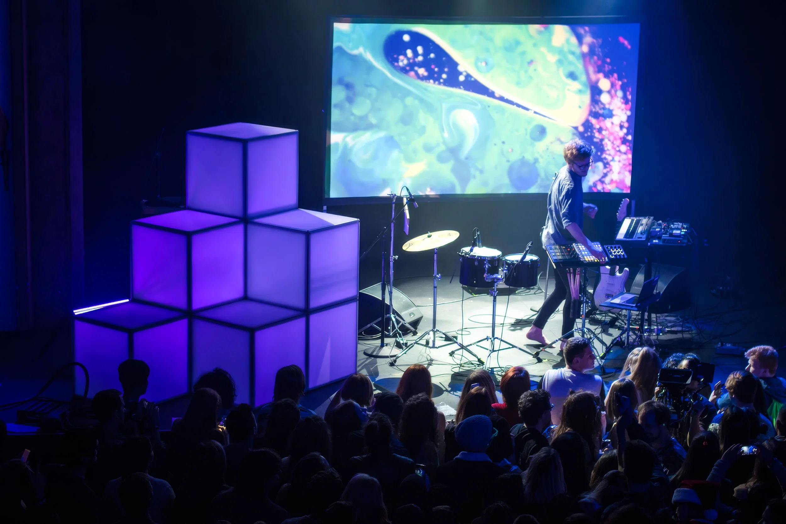 Manatee Commune on stage at the Neptune Theatre in Seattle, violet lit cubes stacked beside custom visuals on the screen