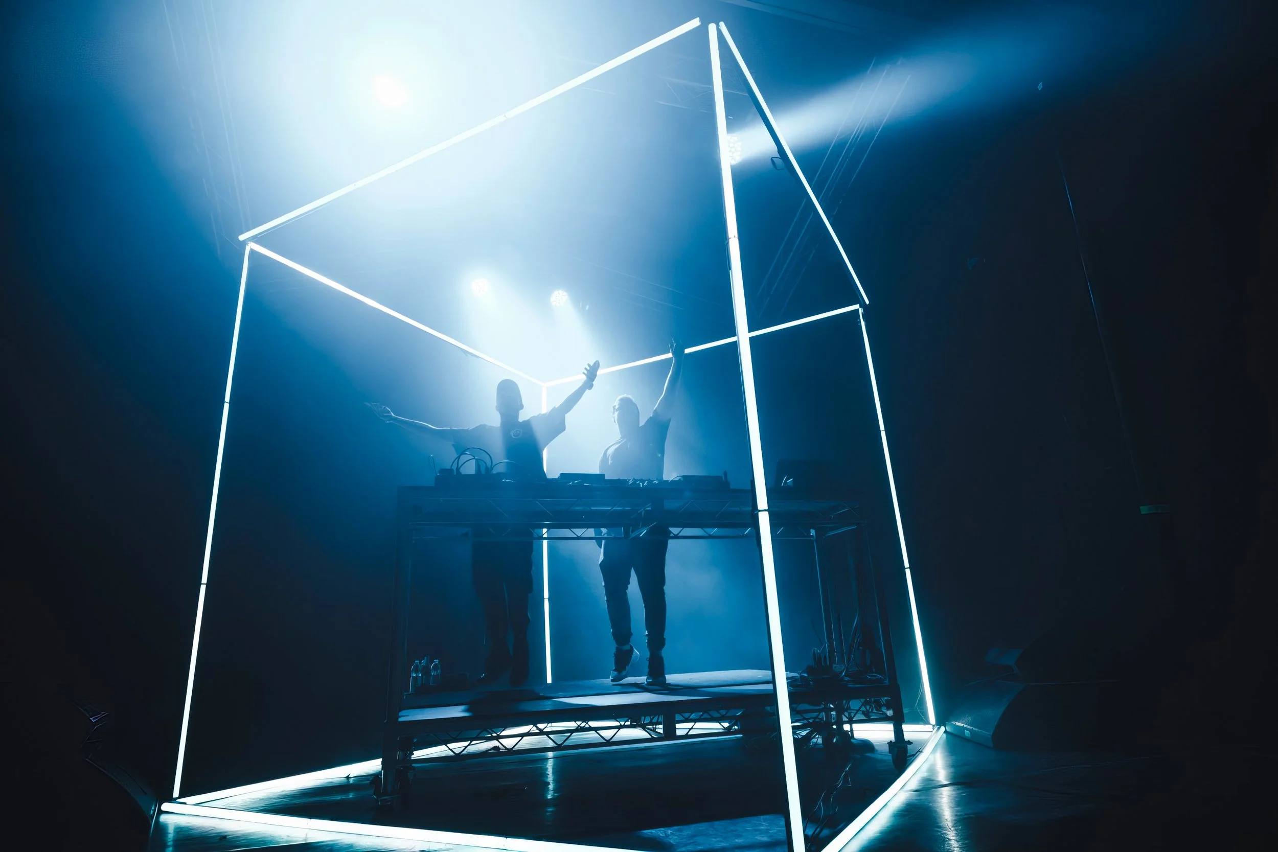 DROELOE silhouetted inside the 3 m LED cube on a hazy stage, beams cutting through fog behind the glowing edges.