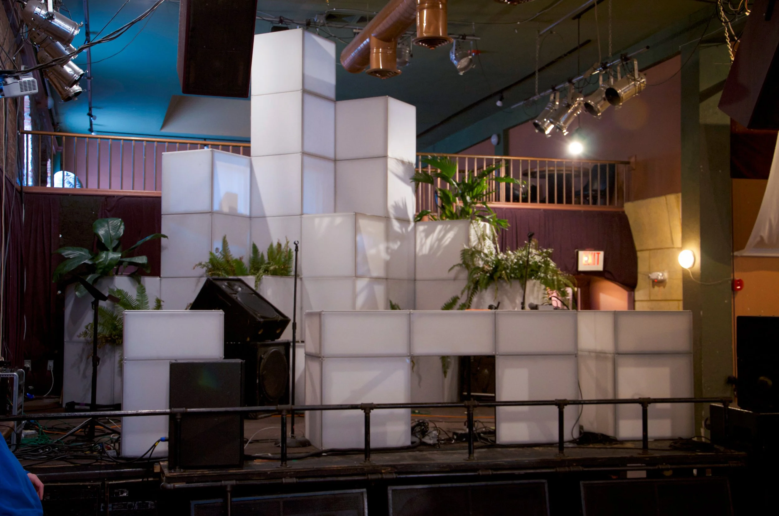 Live From Space stage set in daylight with unlit CUBIX cubes stacked into a hull shape among live plants