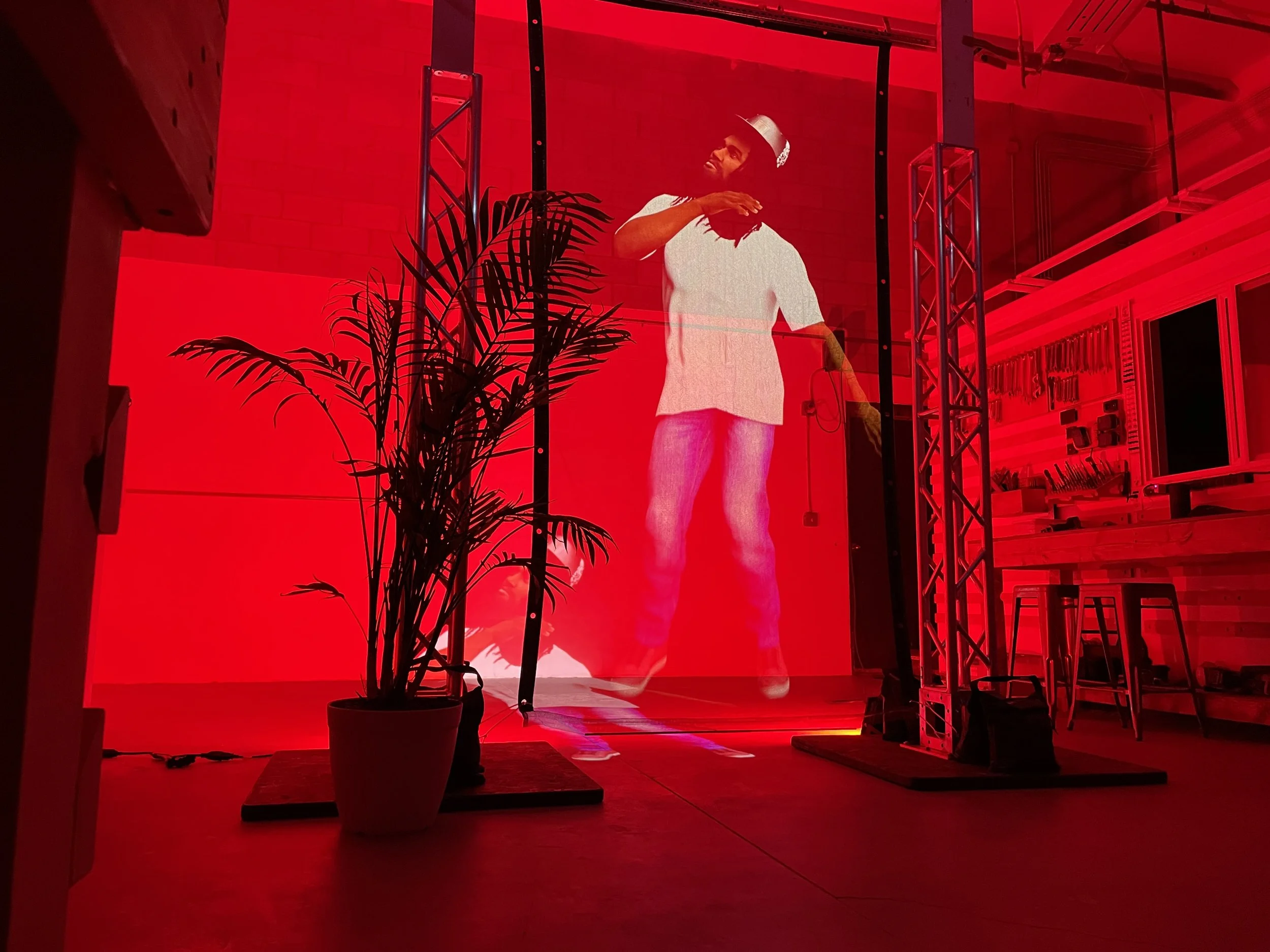 Life size figure projected on a hologram scrim in a red lit studio, pass through image visible on the floor behind it