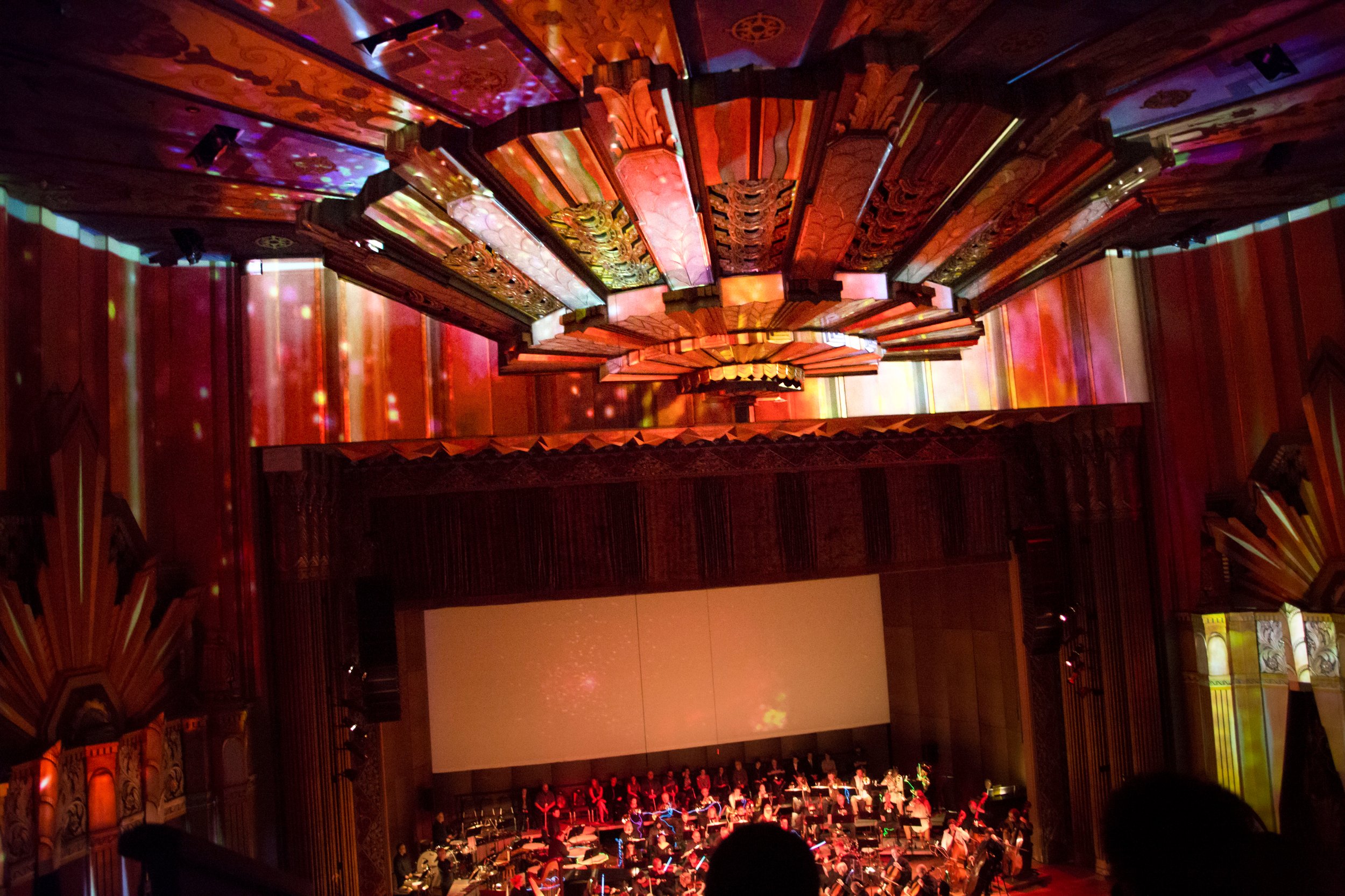 Full orchestra performs beneath live event projection mapping in amber and gold at the Fox Theater in Spokane, Washington