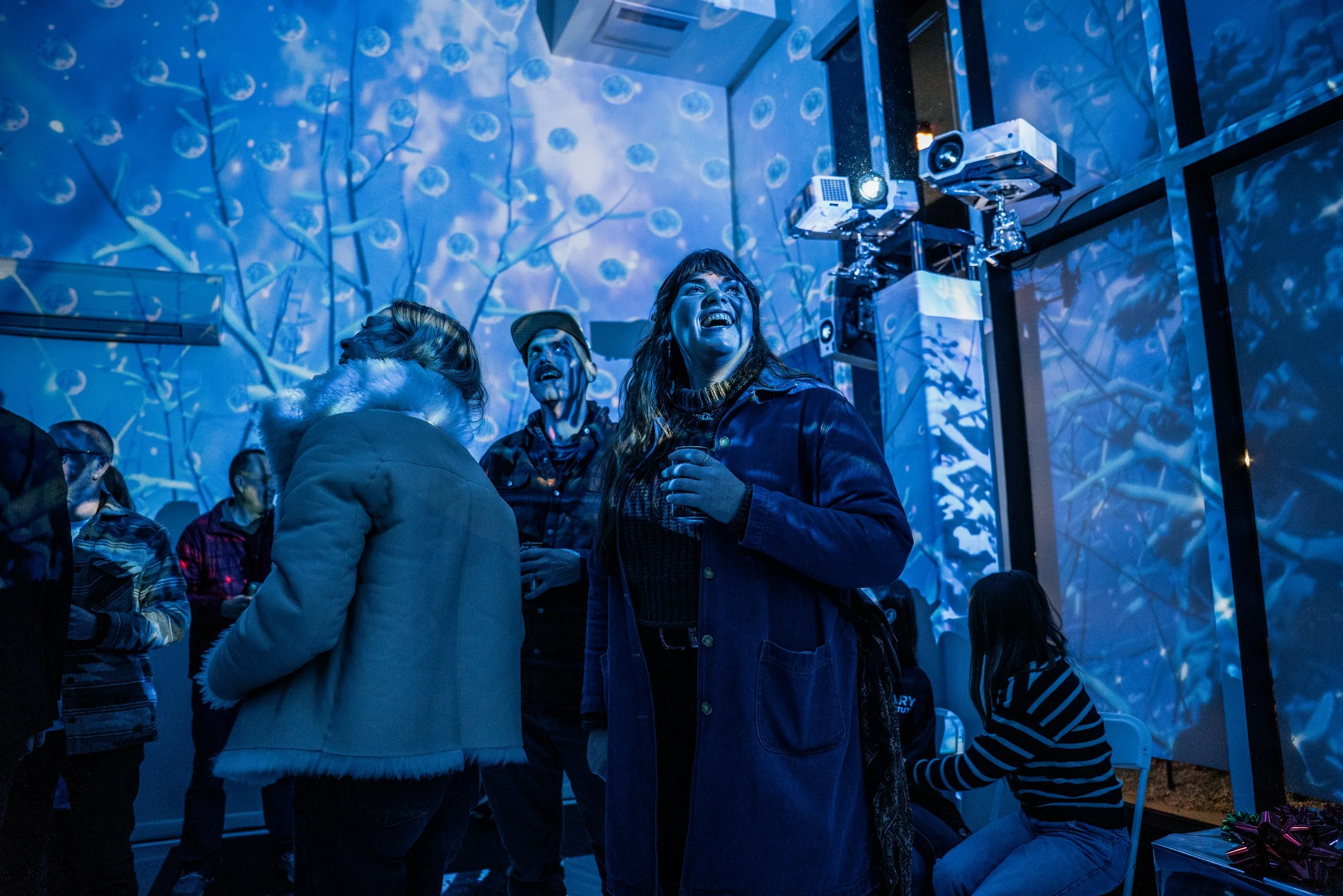 Polaris immersive room at Art Revel Gallery Boise, guests laughing under blue winter branches with a projector above.