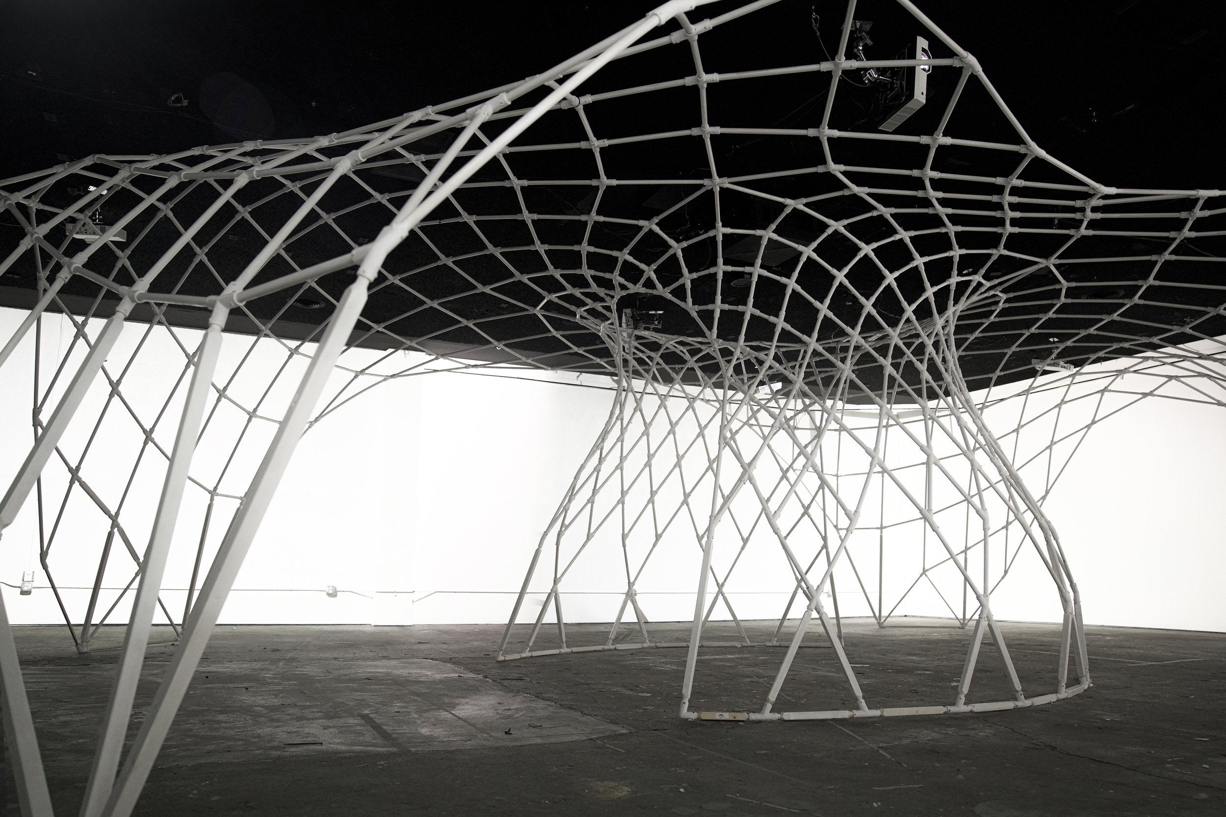 Parametric mesh pavilion in the SKIP building at JUMP in Boise, Idaho, its white lattice arcing over bare concrete.