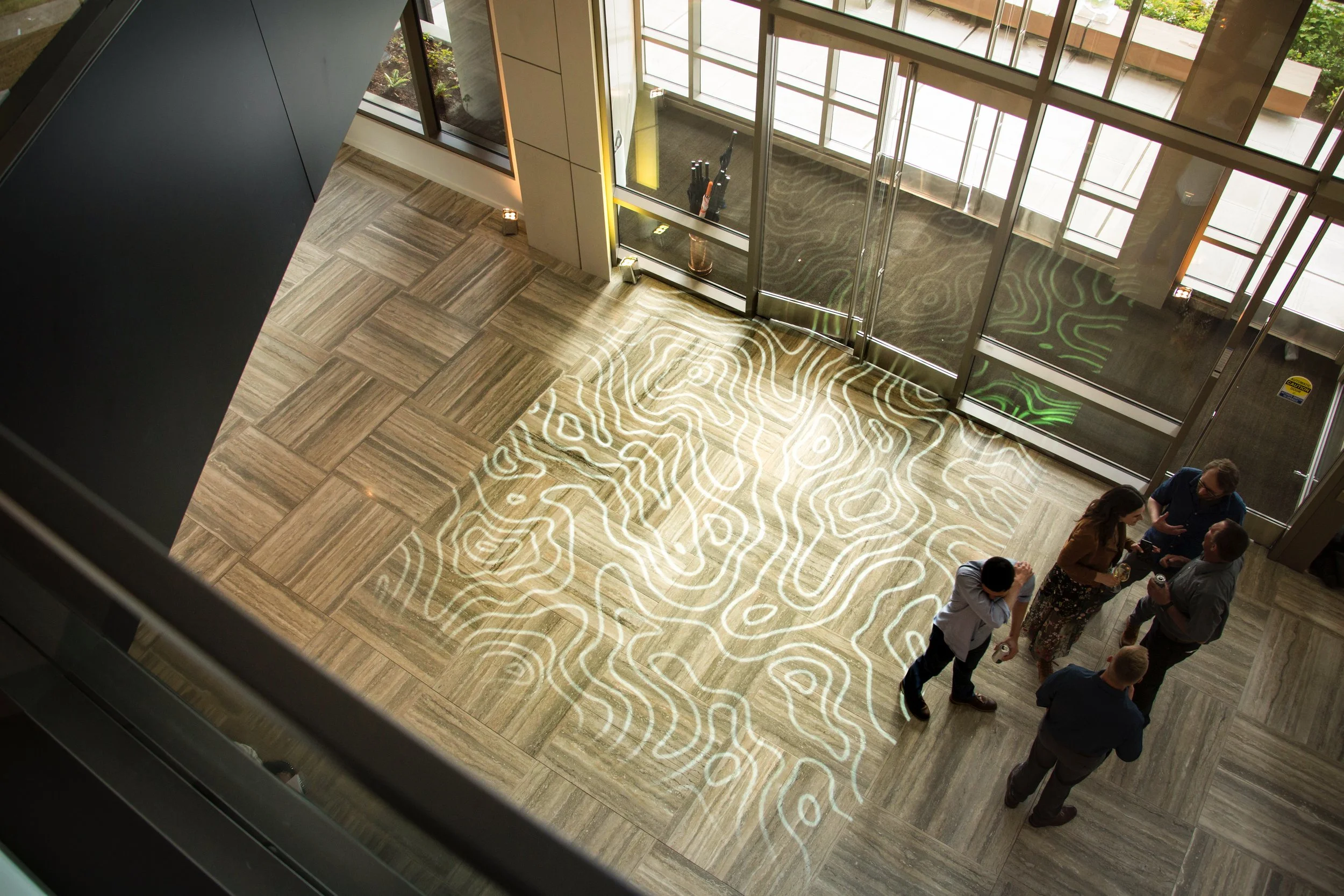 Daylight projection mapping of topographic lines on the floor of the glass lobby at The Collective in Seattle, Washington