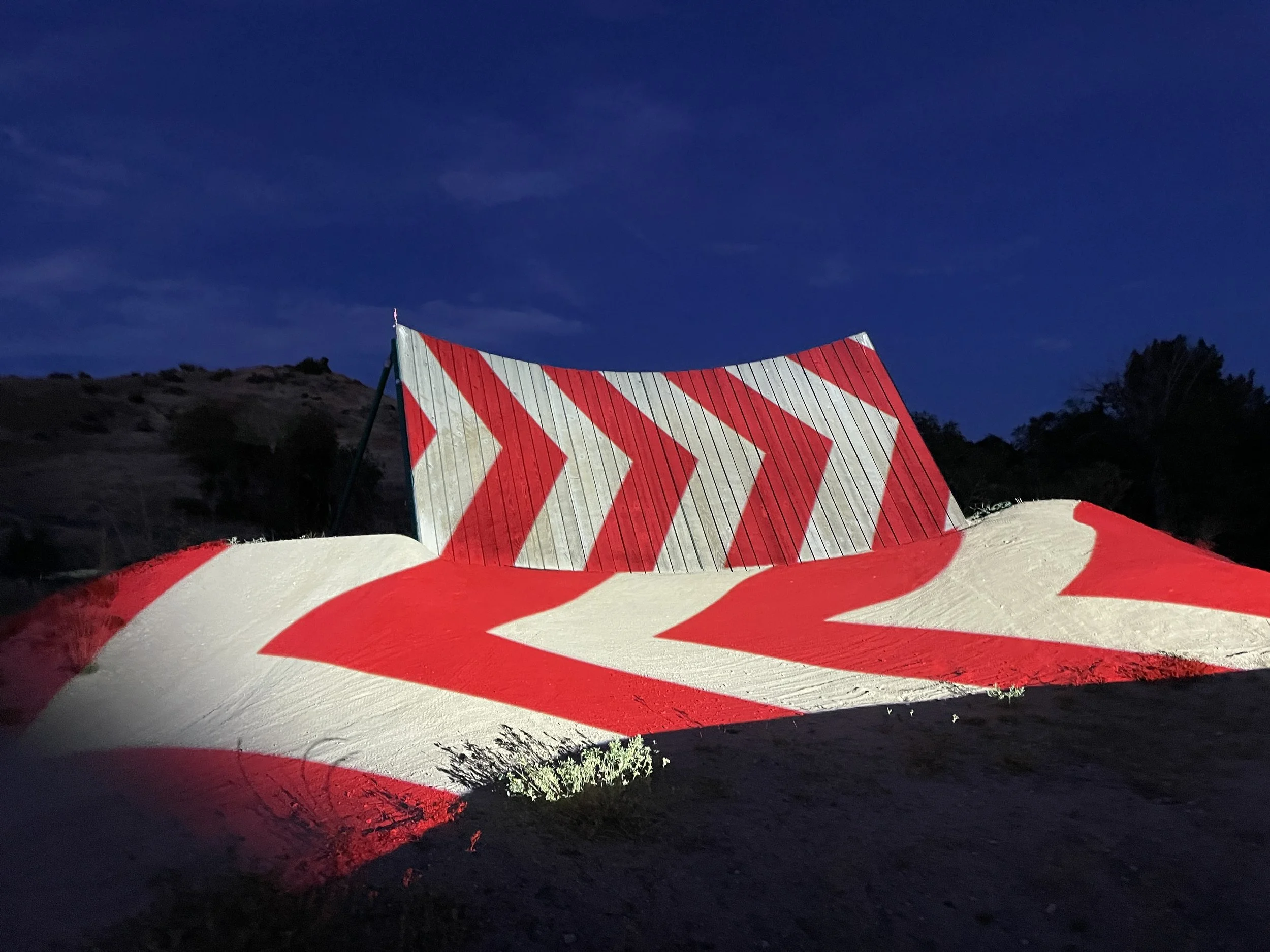 Red chevrons projected across a wall ride and berm at Boise Bike Park, pattern flowing wood to dirt at night.