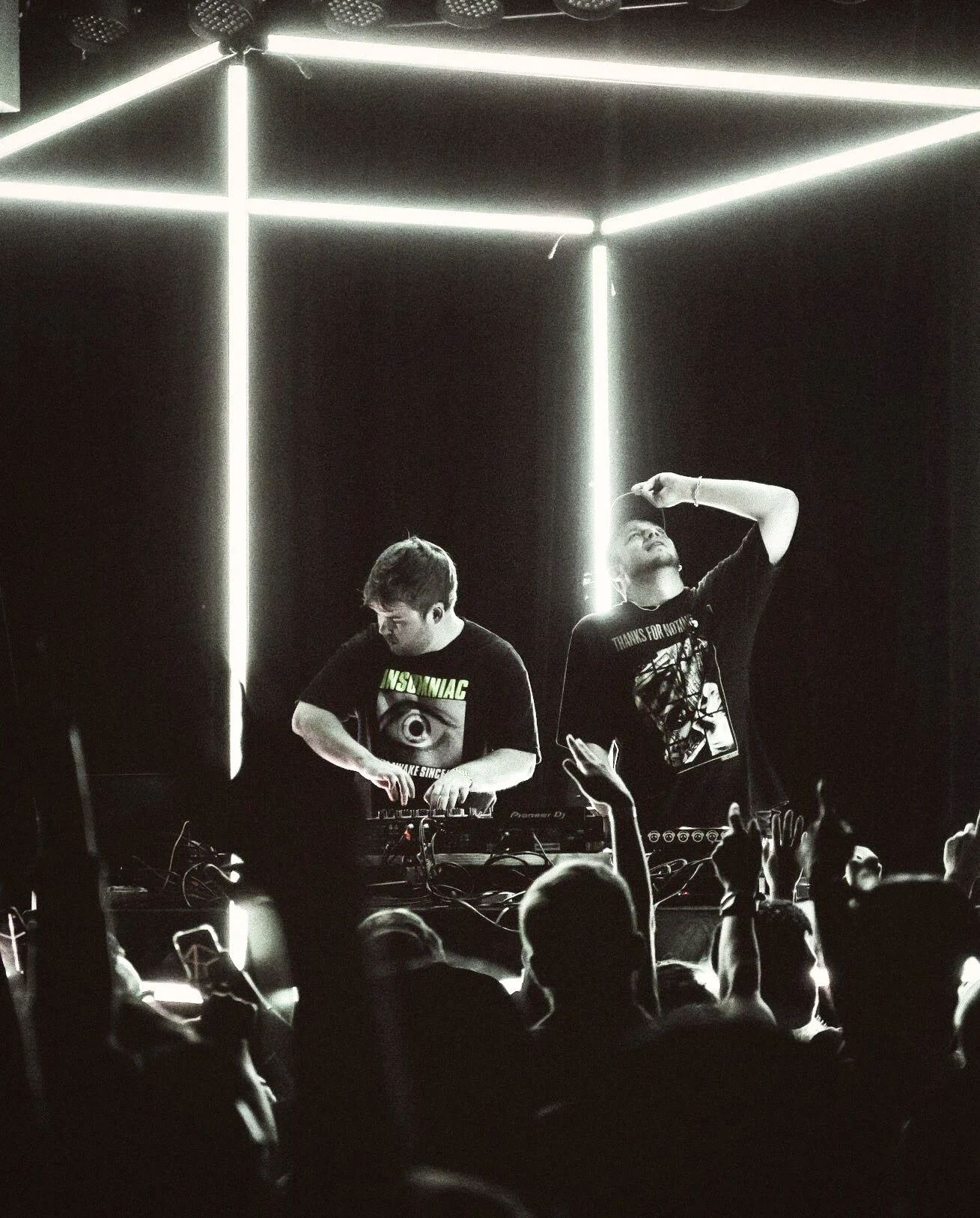 DROELOE performs inside the 3 m LED cube, edges glowing white in a black and white shot as hands rise from the crowd below.