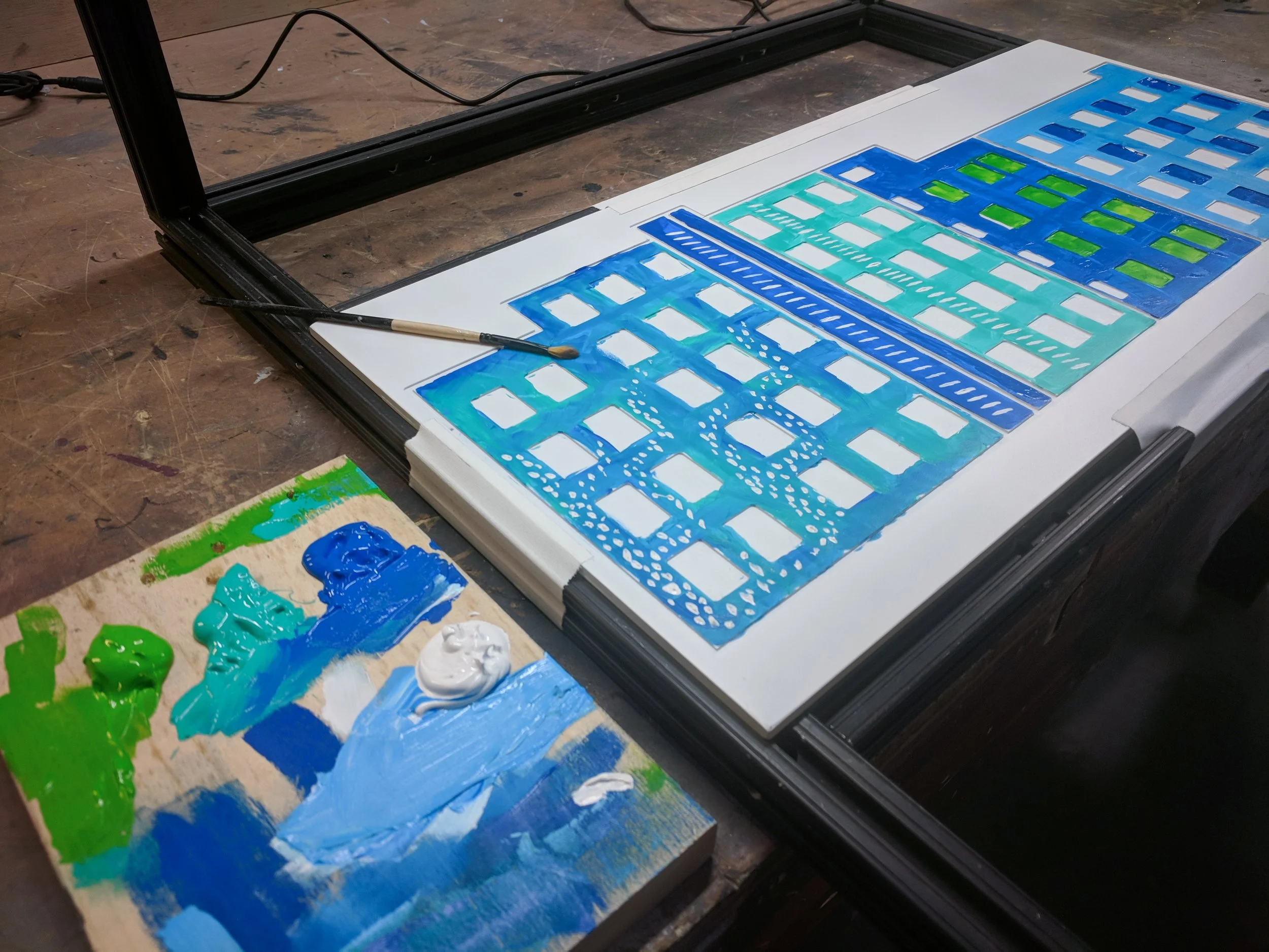 The Herald custom visuals in Bellingham, hand painted facade artwork in blue and green drying beside a palette.