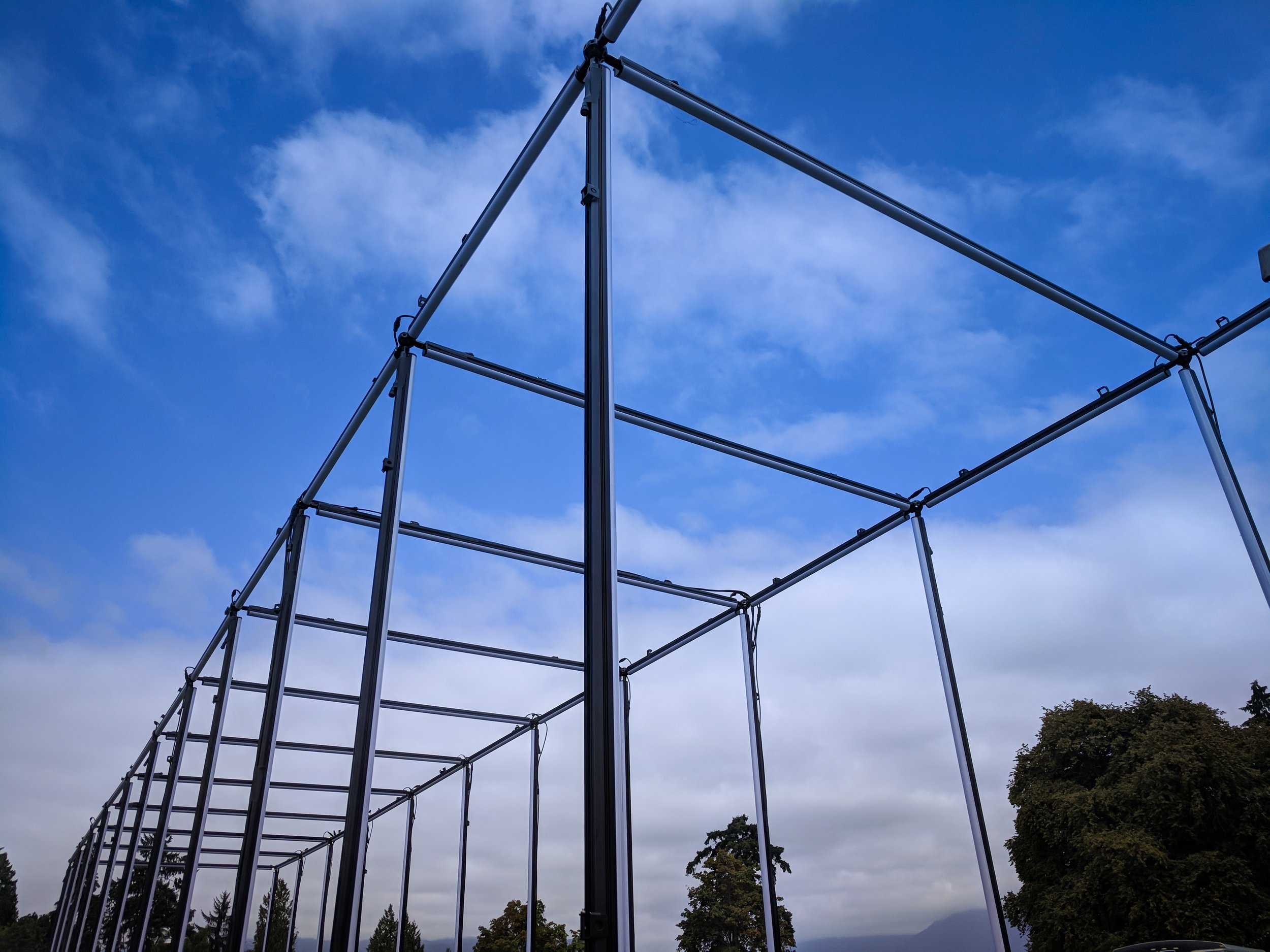 lululemon SeaWheeze LED tunnel structure, bare wireframe truss against blue sky before daytime install