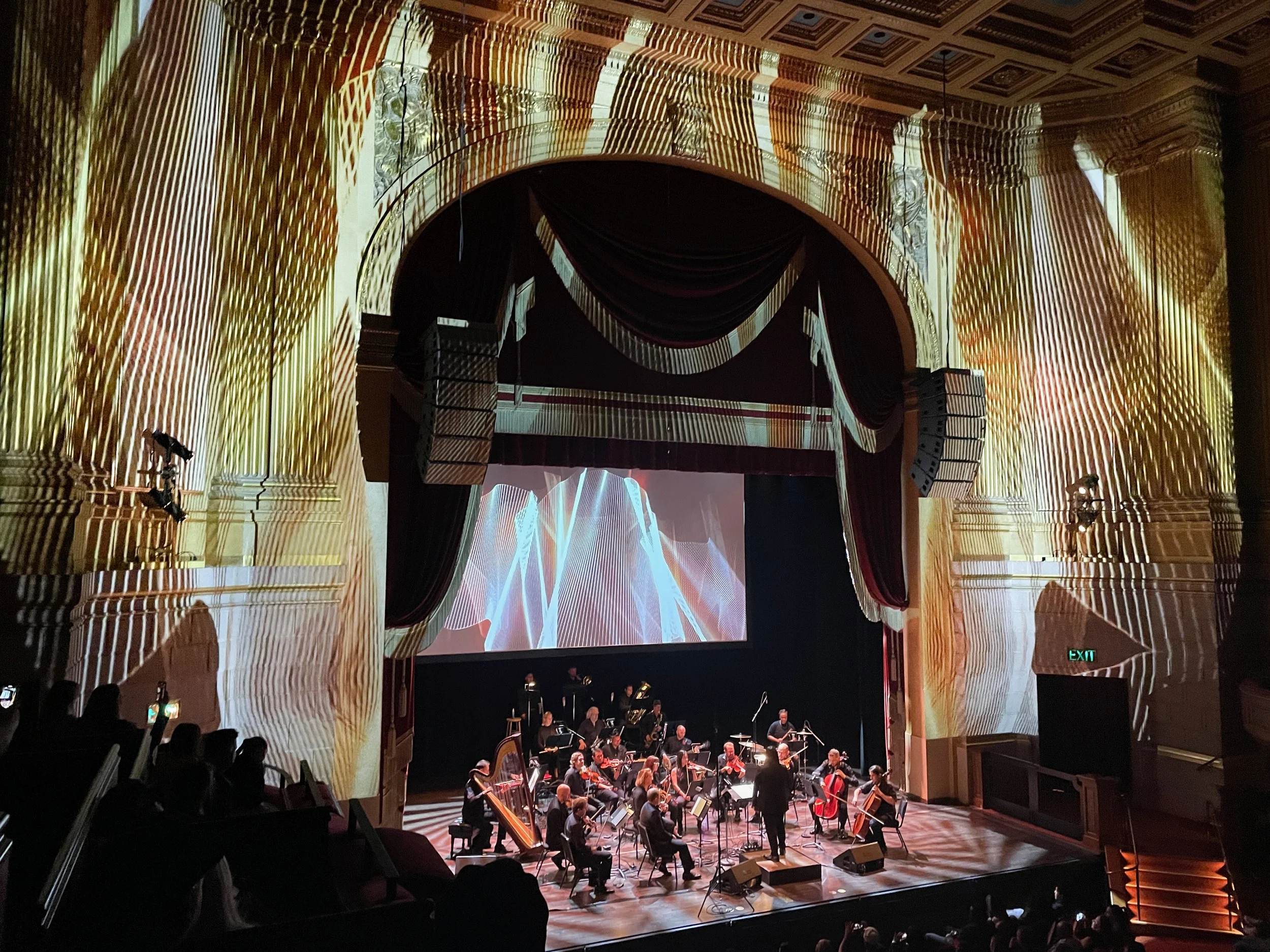 Herbst Theatre interior projection mapping in San Francisco, orchestra performing beneath a light mapped proscenium arch