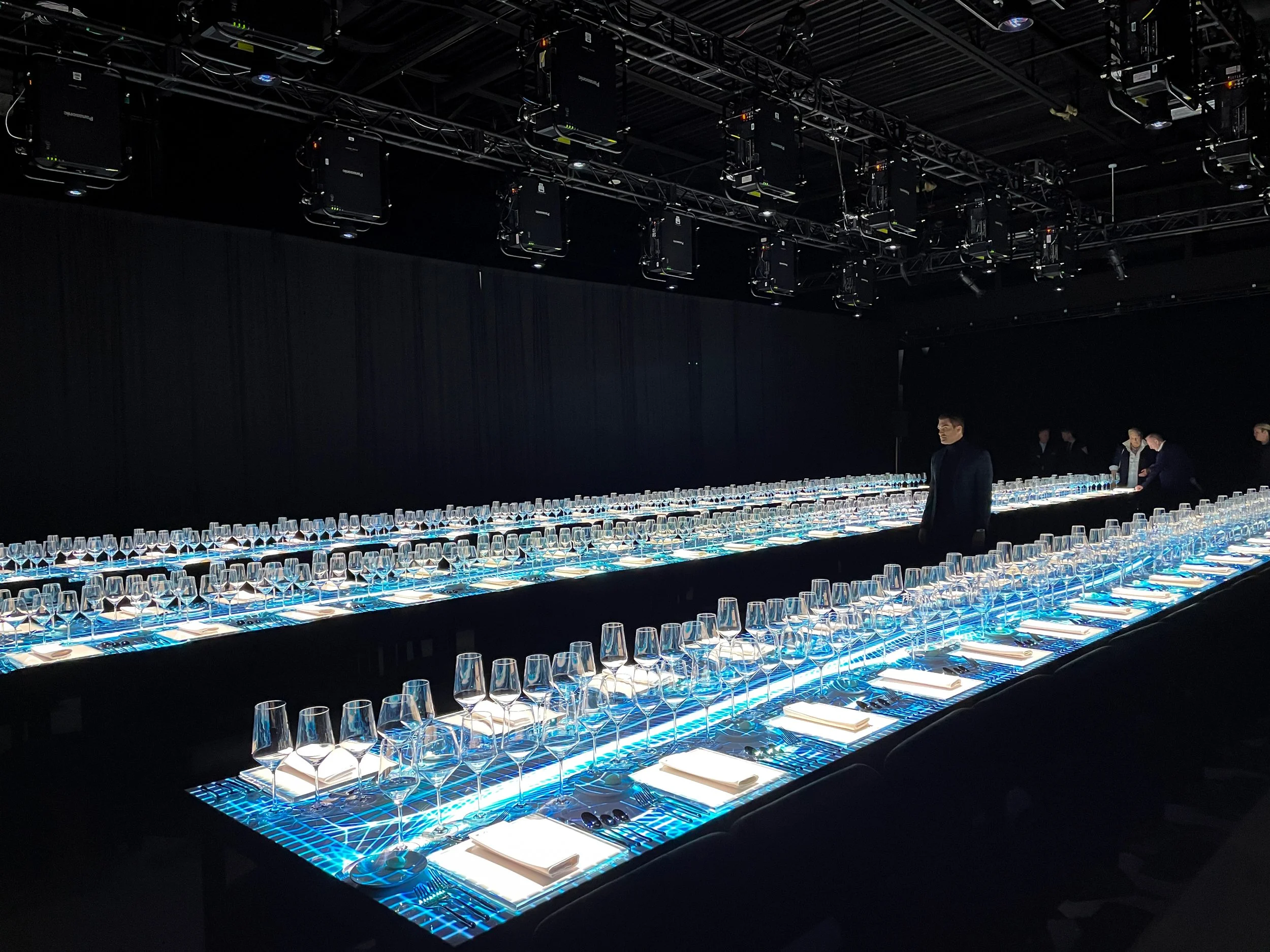 Immersive projection dining setup in a blackout venue with 2 long blue lit tables running the length of the room
